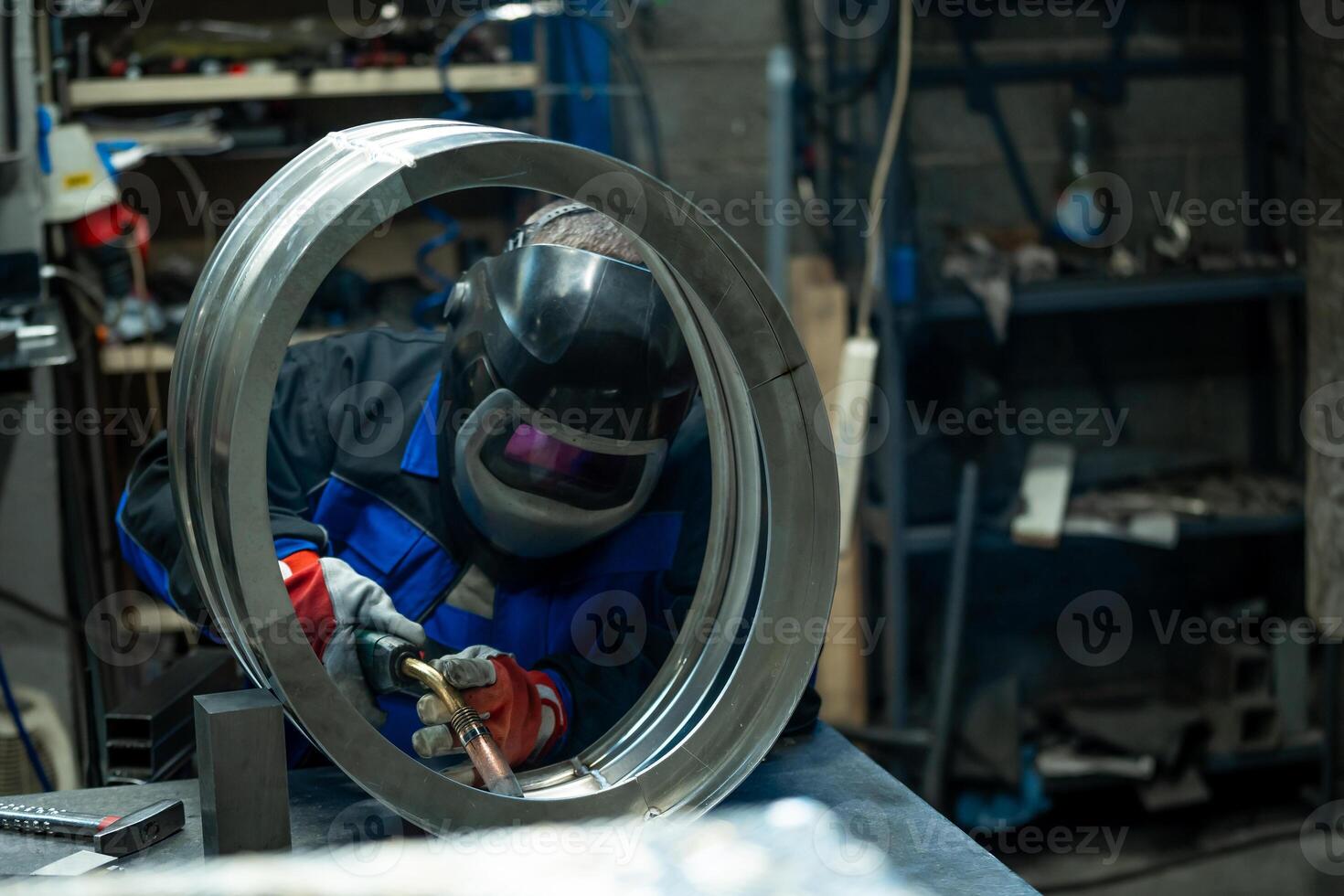 Welder skillfully working on a large metal ring, carefully welding joints in a well equipped workshop. photo