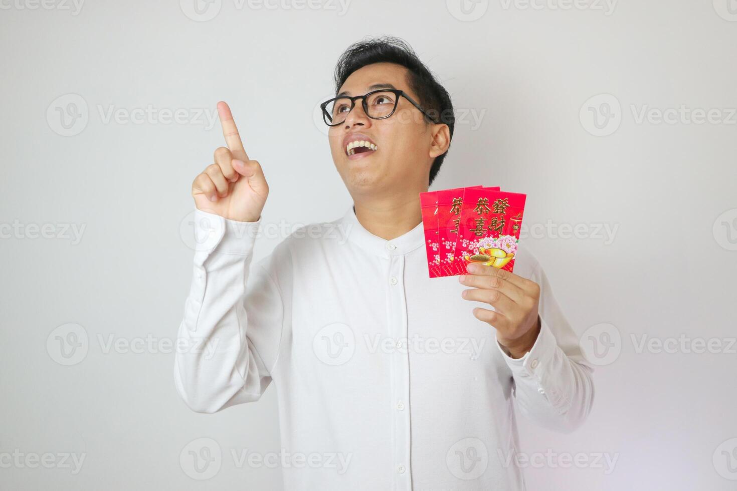 Happy Chinese new year. Asian man pointing and holding red packet monetary gift isolated on white background. Show good luck, greetings, and congratulations. photo