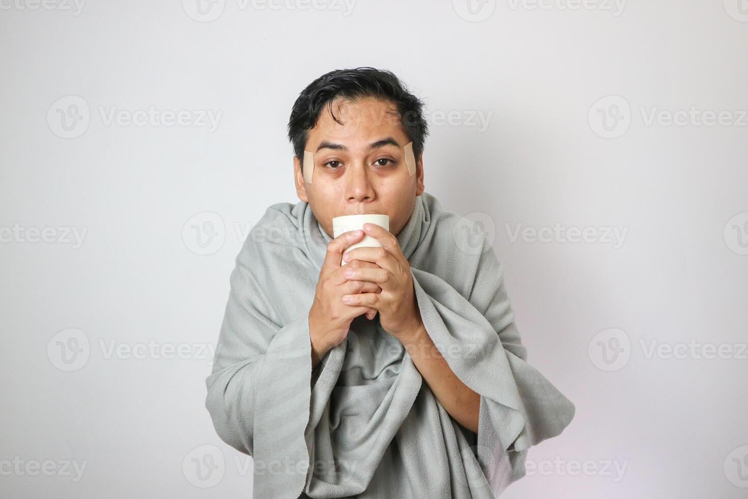 Wrapped in the warm blanket, sick, man with a red nose snotty and drinking warm healing tea photo