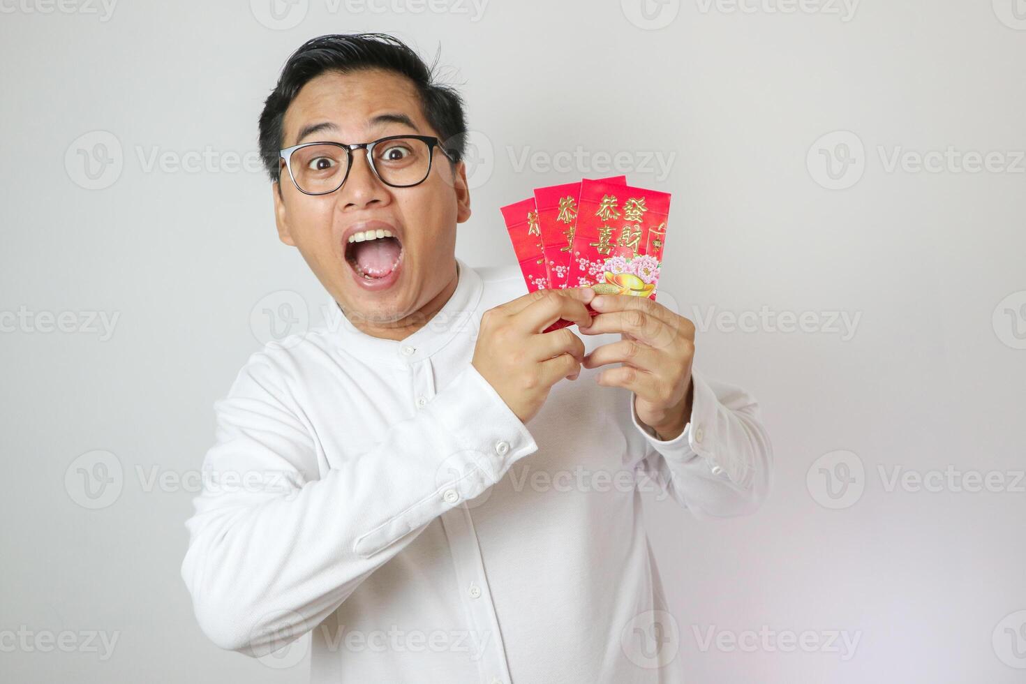 Shocked face of Asian man wearing Chinese traditional cloth called Cheongsam while pulling amounts of money from an angpao on white background photo