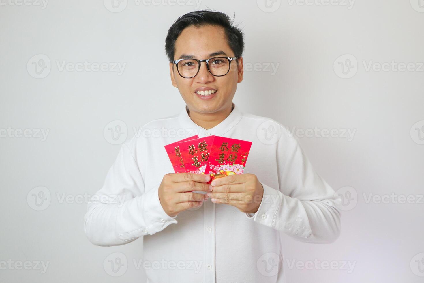 Happy Chinese new year. Asian man holding angpao or red packet monetary gift isolated on red decoration background. Chinese text means great luck great happy. photo