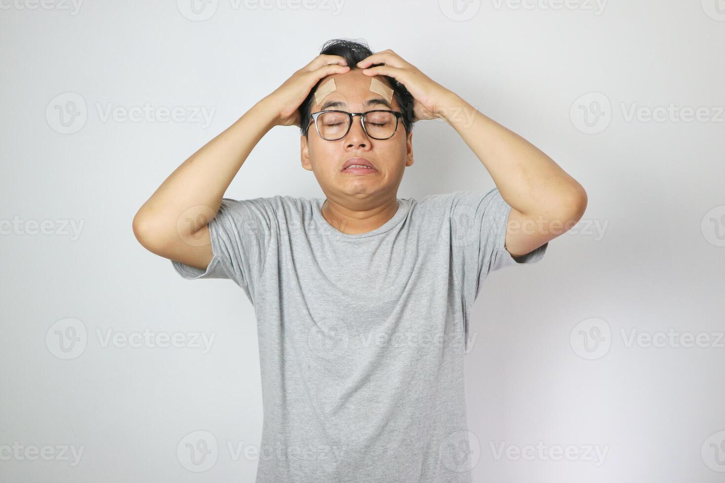 Portrait of young man isolated on gray background, suffering from severe headache, pressing fingers to temples with closed eyes photo