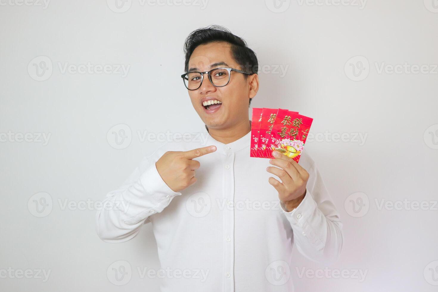 Asian man wearing Cheongsam or Chinese traditional cloth is holding and pointing angpao or red monetary gift on white background. Gong Xi Fa Cai. photo