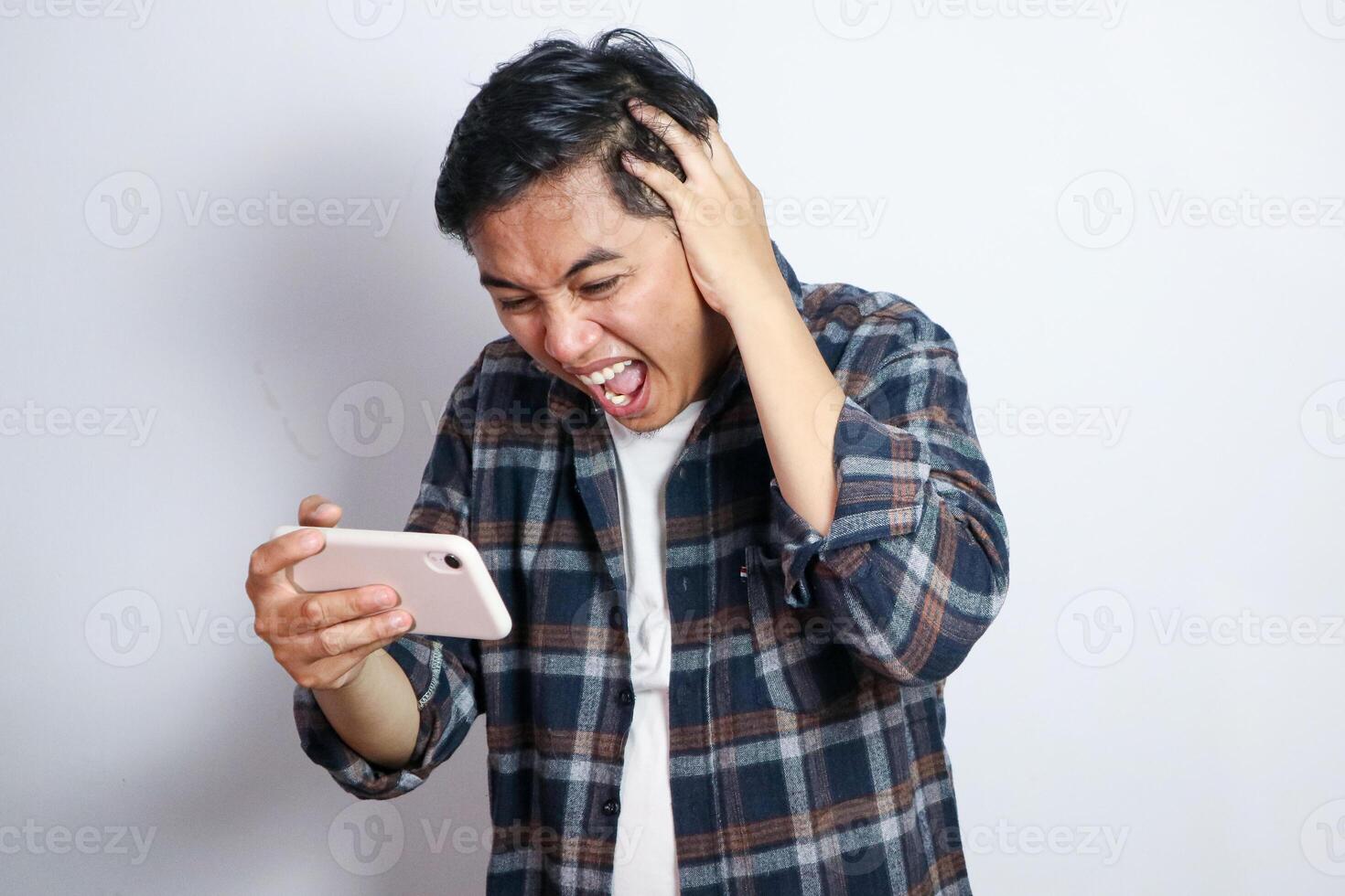Oh No. Portrait of emotional shocked asian guy holding and using smartphone, seeing surprising news, photos or message. Surprised man grabbing head isolated over white studio background wall