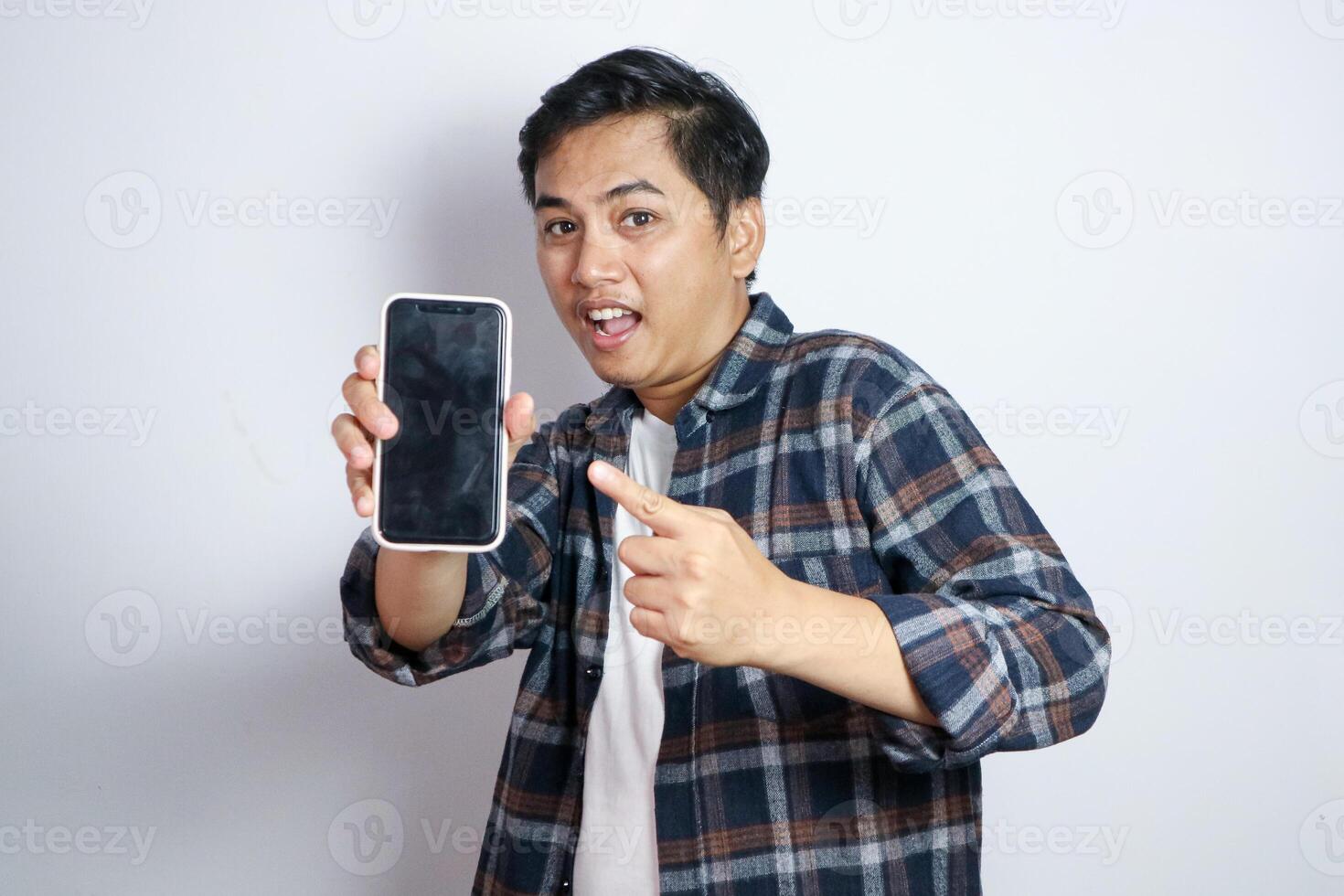 Happy Asian man showing and pointing finger to smartphone mockup of blank screen isolated on white background. photo