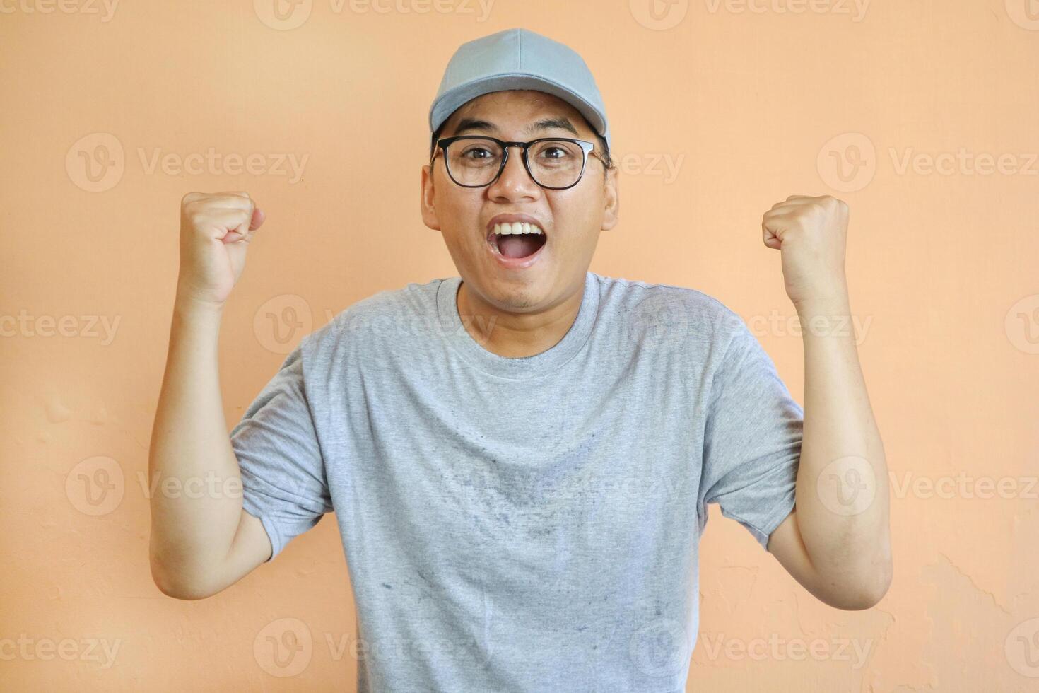 Excited and happy asian courier in grey uniform shouting yes and rejoicing, fist pump as celebrating great news, triumphing over white background. Delivery man looking euphoric and winning photo