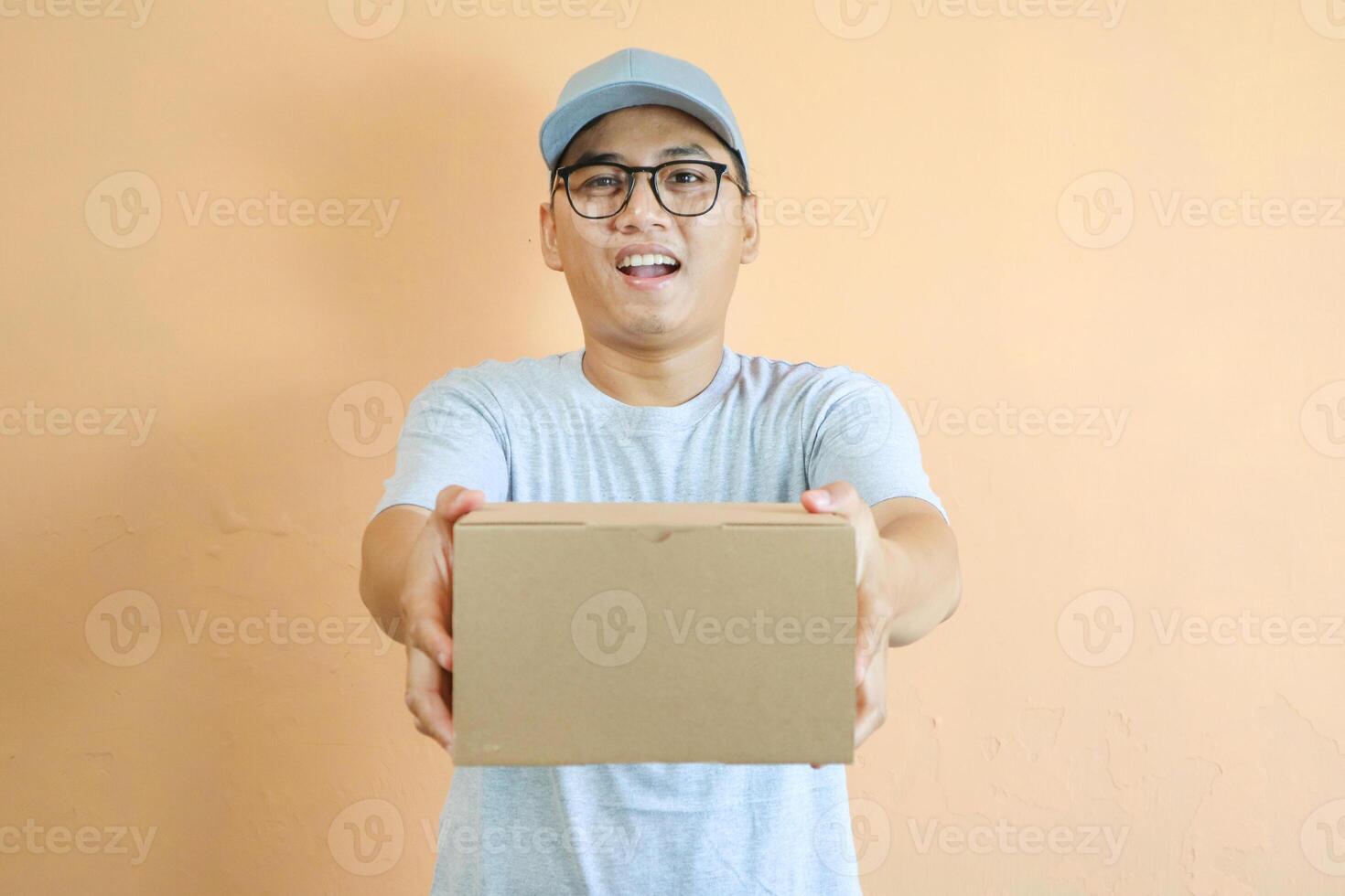 Asian Young delivery man wearing grey shirt on yellow background studio holding package box photo