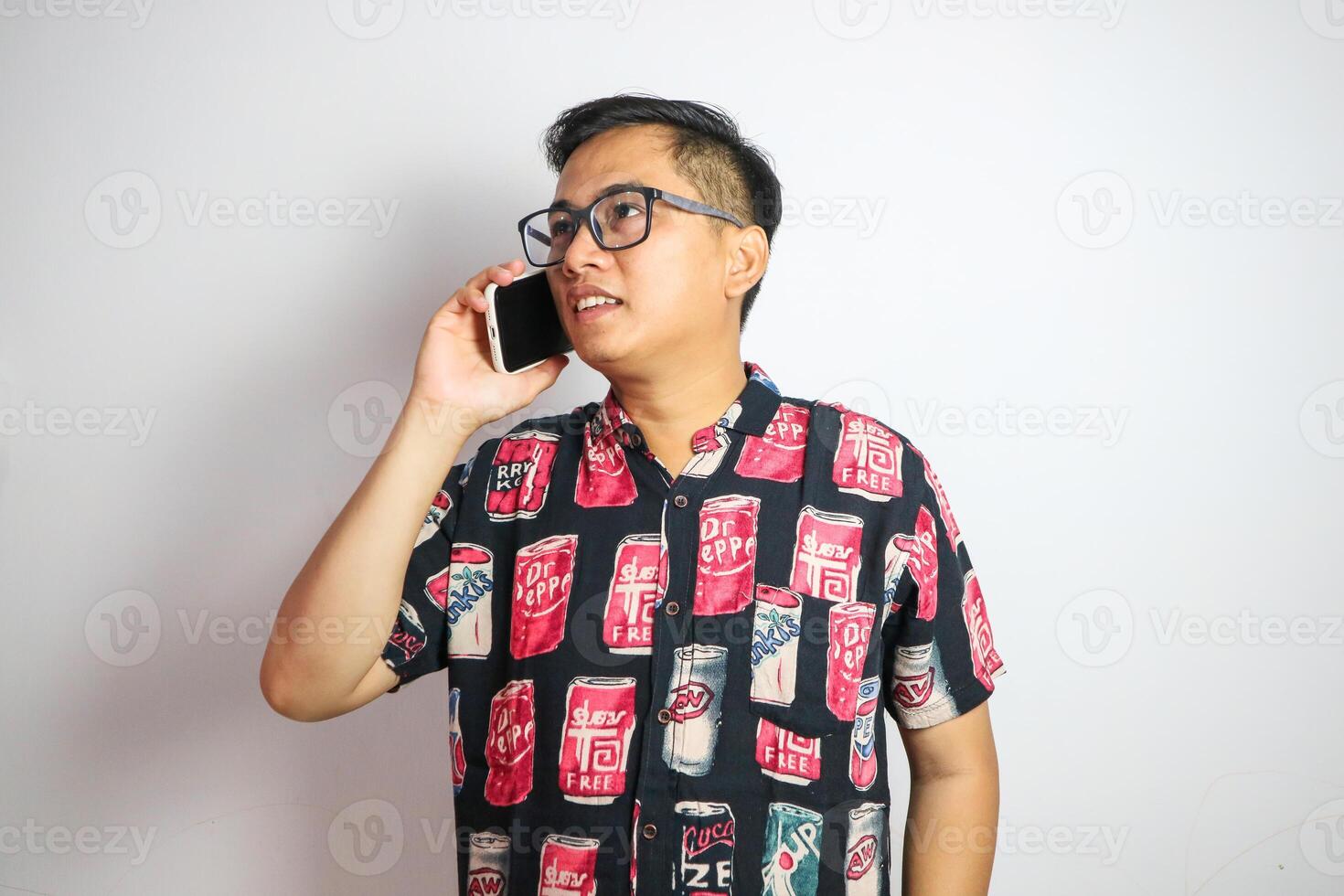 A fun, excited Asian man tourist in summer clothes and sunglasses is talking on the phone with someone, posing with a luggage on an isolated white background. summer vacation, beach trip, journey photo