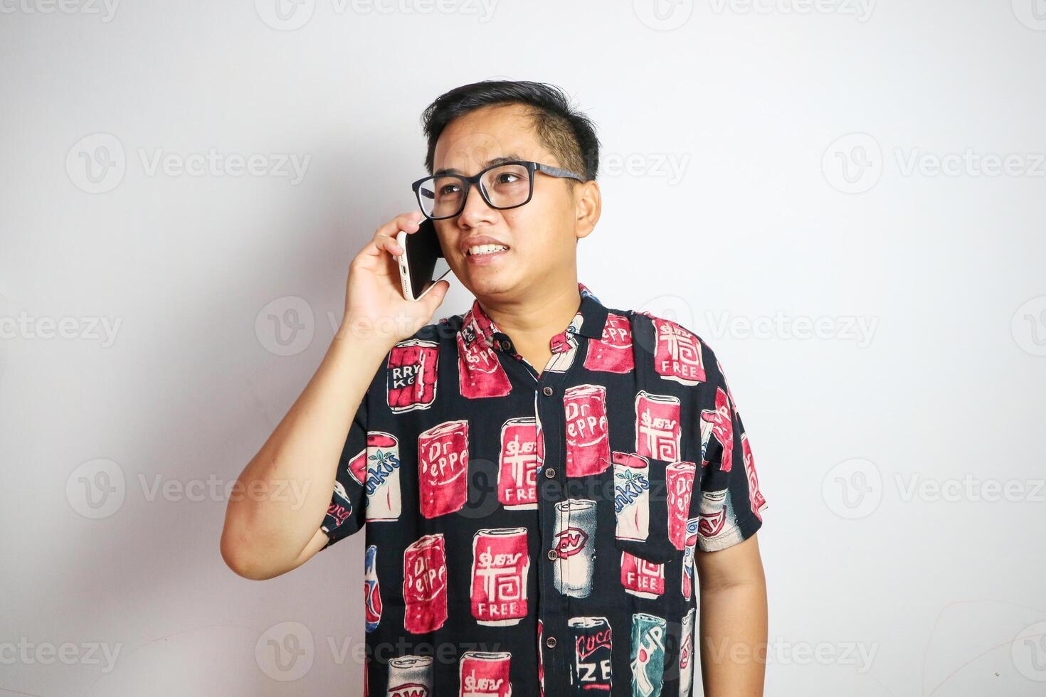 A fun, excited Asian man tourist in summer clothes and sunglasses is talking on the phone with someone, posing with a luggage on an isolated white background. summer vacation, beach trip, journey photo