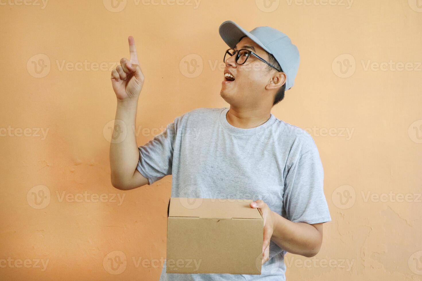 Asian delivery man is pointing at empty copy space while holding a cardboard box package parcel, Isolated on a white background, advertisements, promotions, or announcements, delivery services photo
