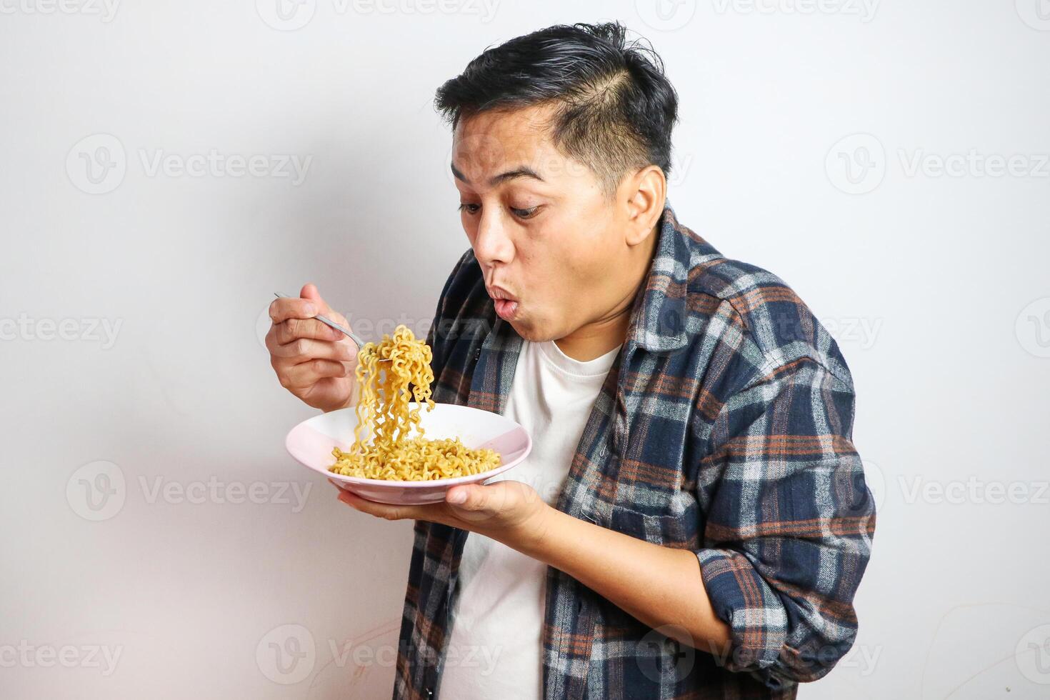 Young handsome trendy asian man eating yummy hot and spicy instant noodle using fork isolated on white background. Asian guy servile end of the month with cheap food. photo