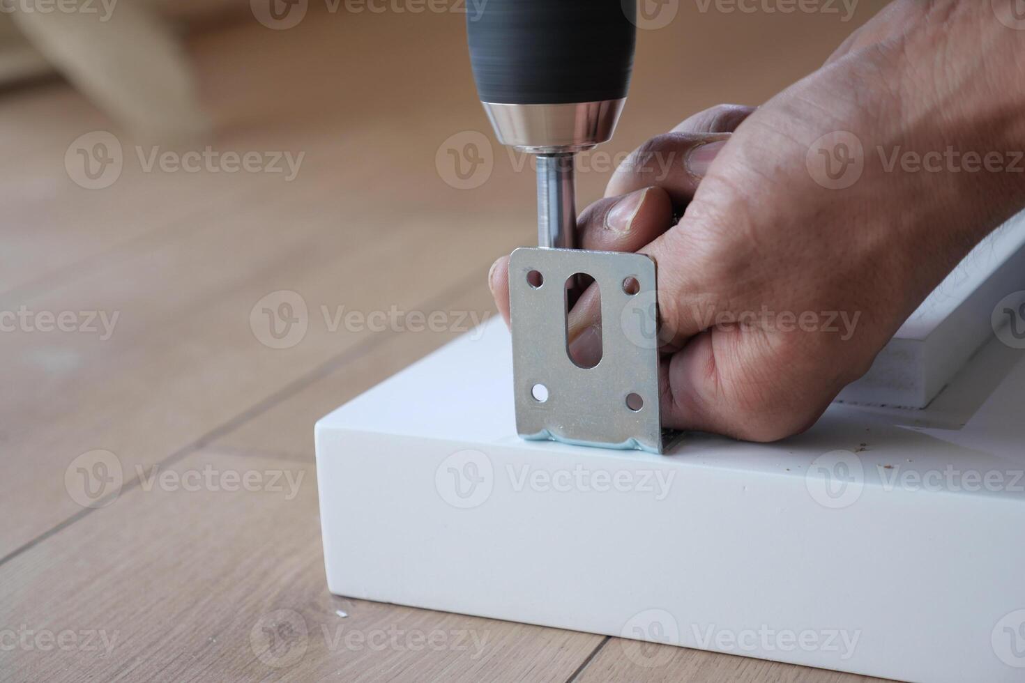 A person is using a power drill effectively to secure a metal bracket onto a clean white surface photo
