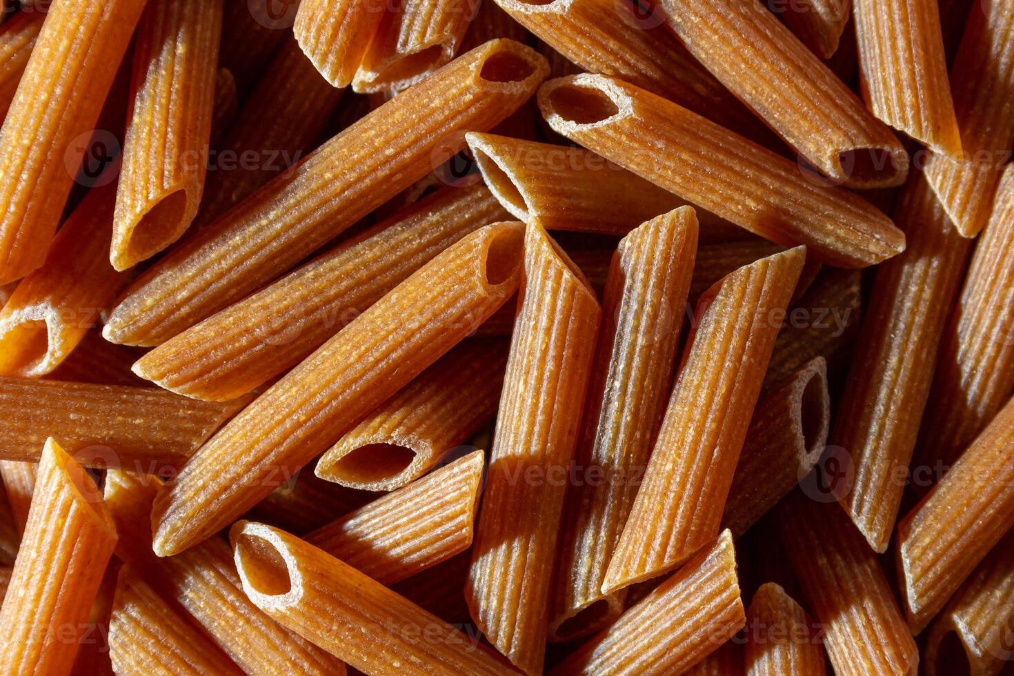 Uncooked Whole Grain Penne Rigate Pasta. A Culinary Canvas of Whole Wheat Macaroni, Creating a Lively and Textured Background for Gourmet Cooking. Whole Grain Dry Pasta. Whole Wheat Raw Macaroni photo