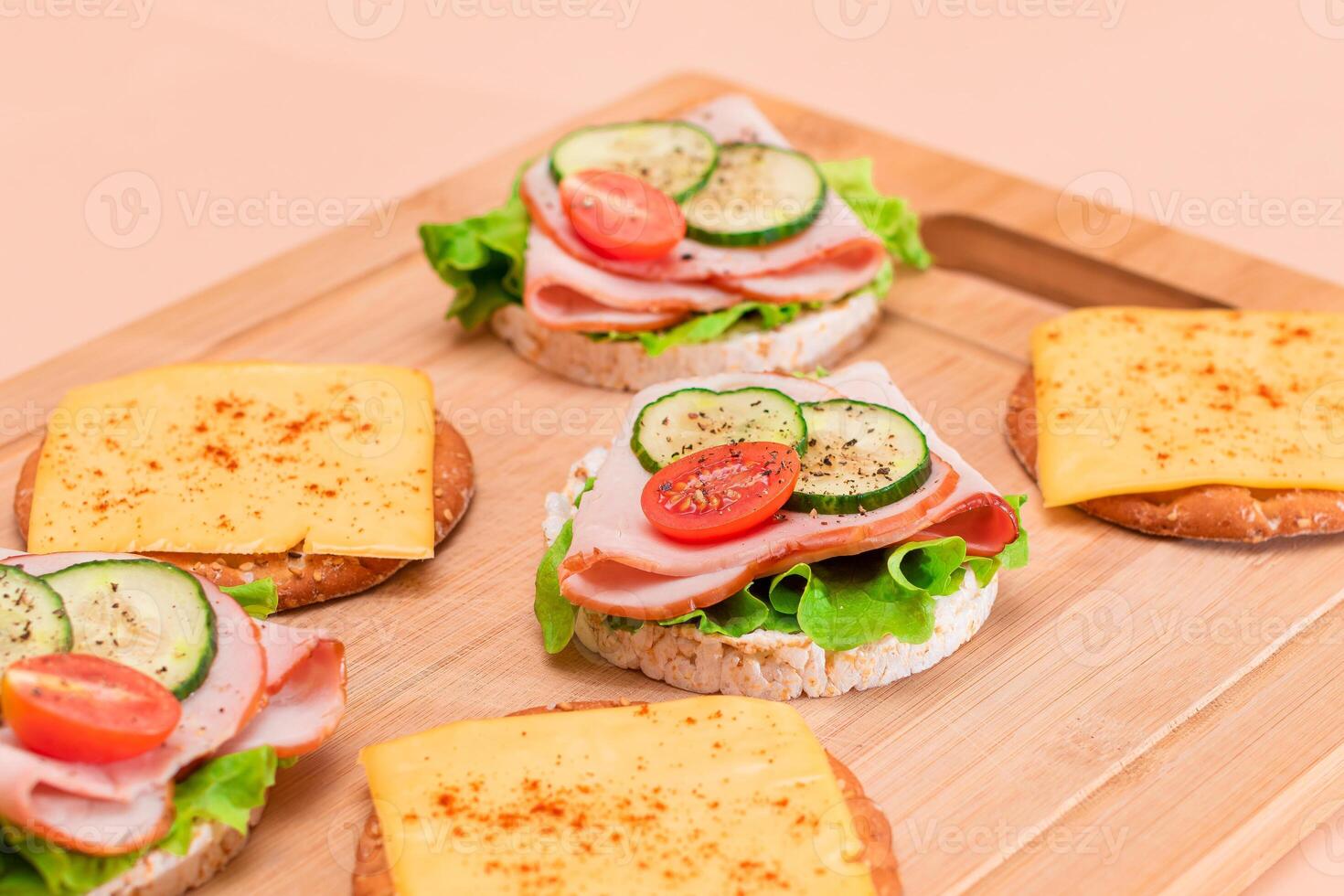 Light Breakfast. Quick and Healthy Sandwiches. Rice Cakes with Ham, Tomato, Fresh Cucumber, Green Salad and Cheese on Wooden Cutting Board. Beige Background photo