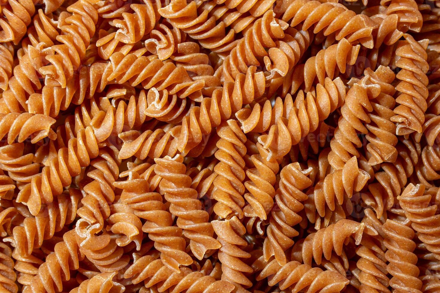 Uncooked Whole Grain Fusilli Pasta. A Culinary Canvas of Whole Wheat Spirals, Creating a Lively and Textured Background for Gourmet Cooking. Whole Grain Twisted Dry Pasta. Whole Wheat Raw Macaroni photo