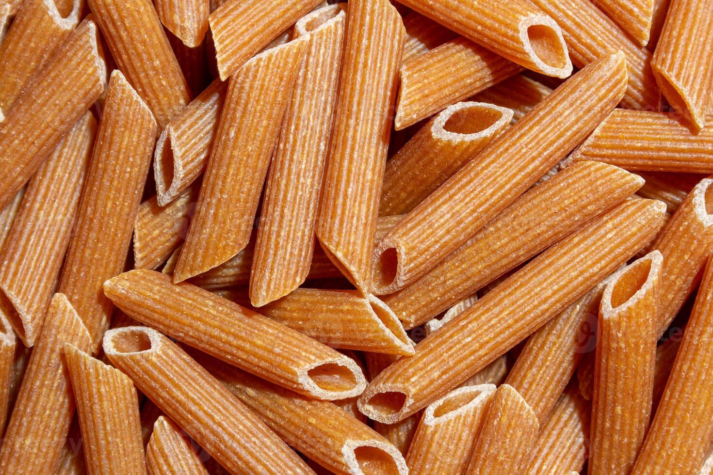 Uncooked Whole Grain Penne Rigate Pasta. A Culinary Canvas of Whole Wheat Macaroni, Creating a Lively and Textured Background for Gourmet Cooking. Whole Grain Dry Pasta. Whole Wheat Raw Macaroni photo