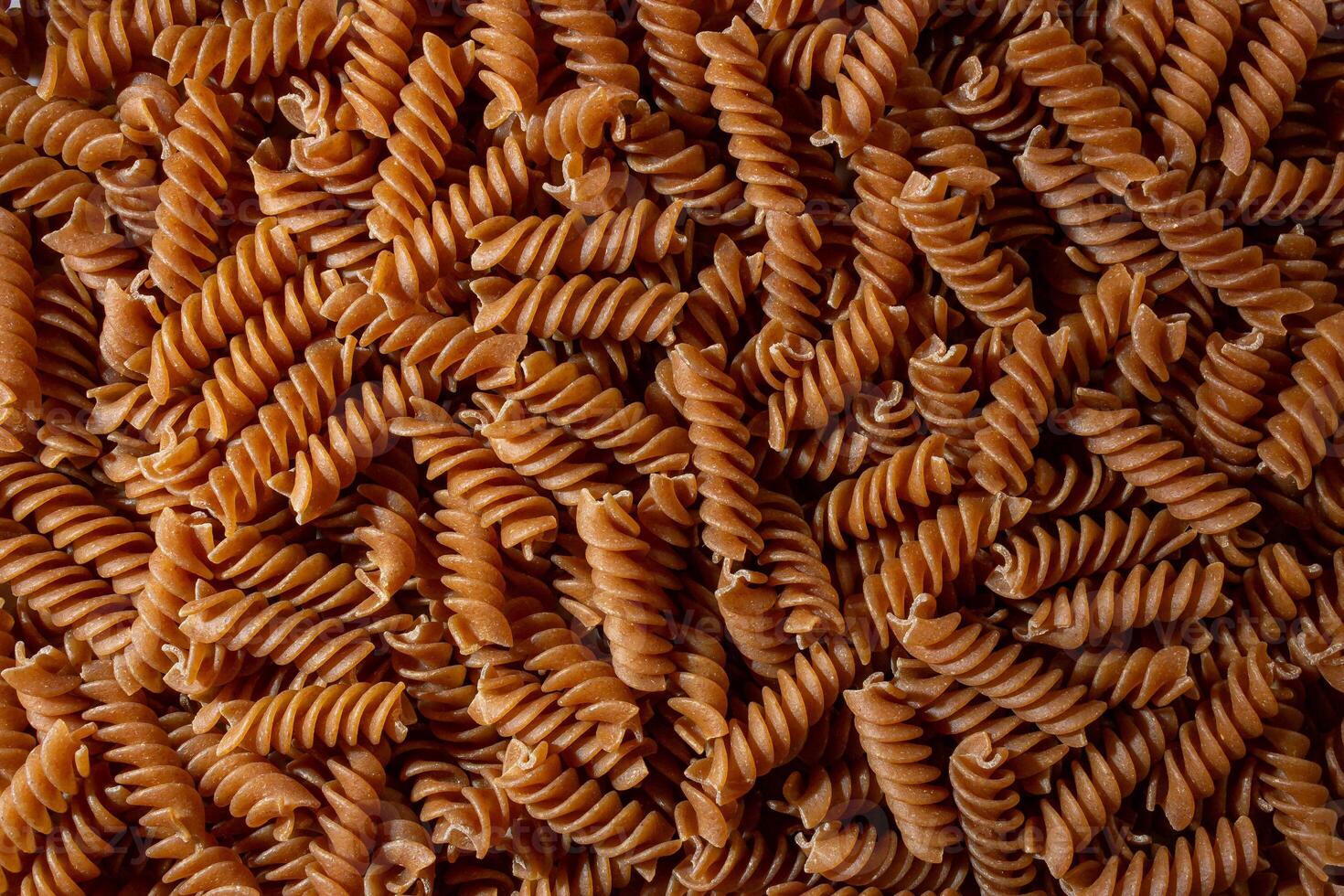 Uncooked Whole Grain Fusilli Pasta. A Culinary Canvas of Whole Wheat Spirals, Creating a Lively and Textured Background for Gourmet Cooking. Whole Grain Twisted Dry Pasta. Whole Wheat Raw Macaroni photo