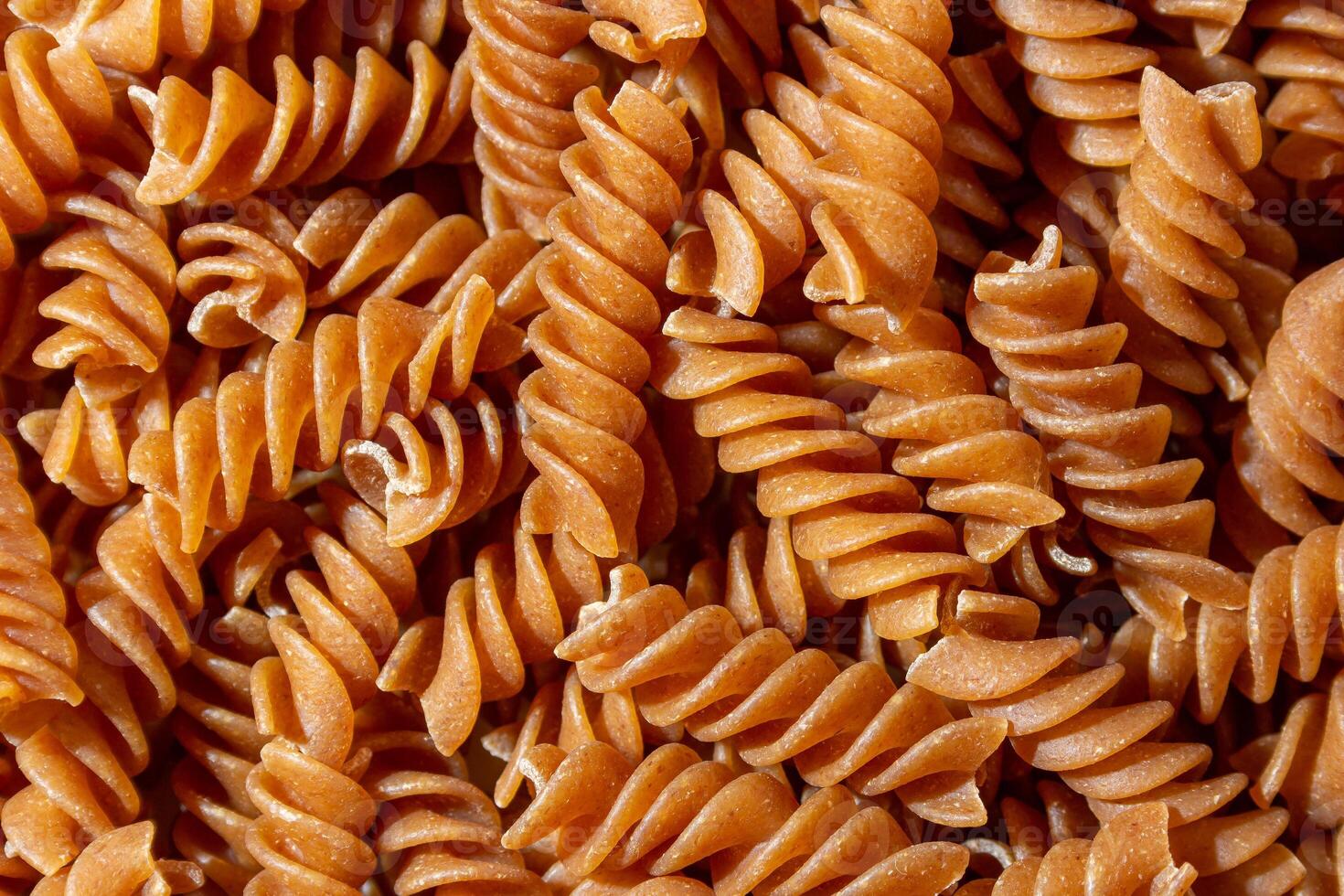 Uncooked Whole Grain Fusilli Pasta. A Culinary Canvas of Whole Wheat Spirals, Creating a Lively and Textured Background for Gourmet Cooking. Whole Grain Twisted Dry Pasta. Whole Wheat Raw Macaroni photo