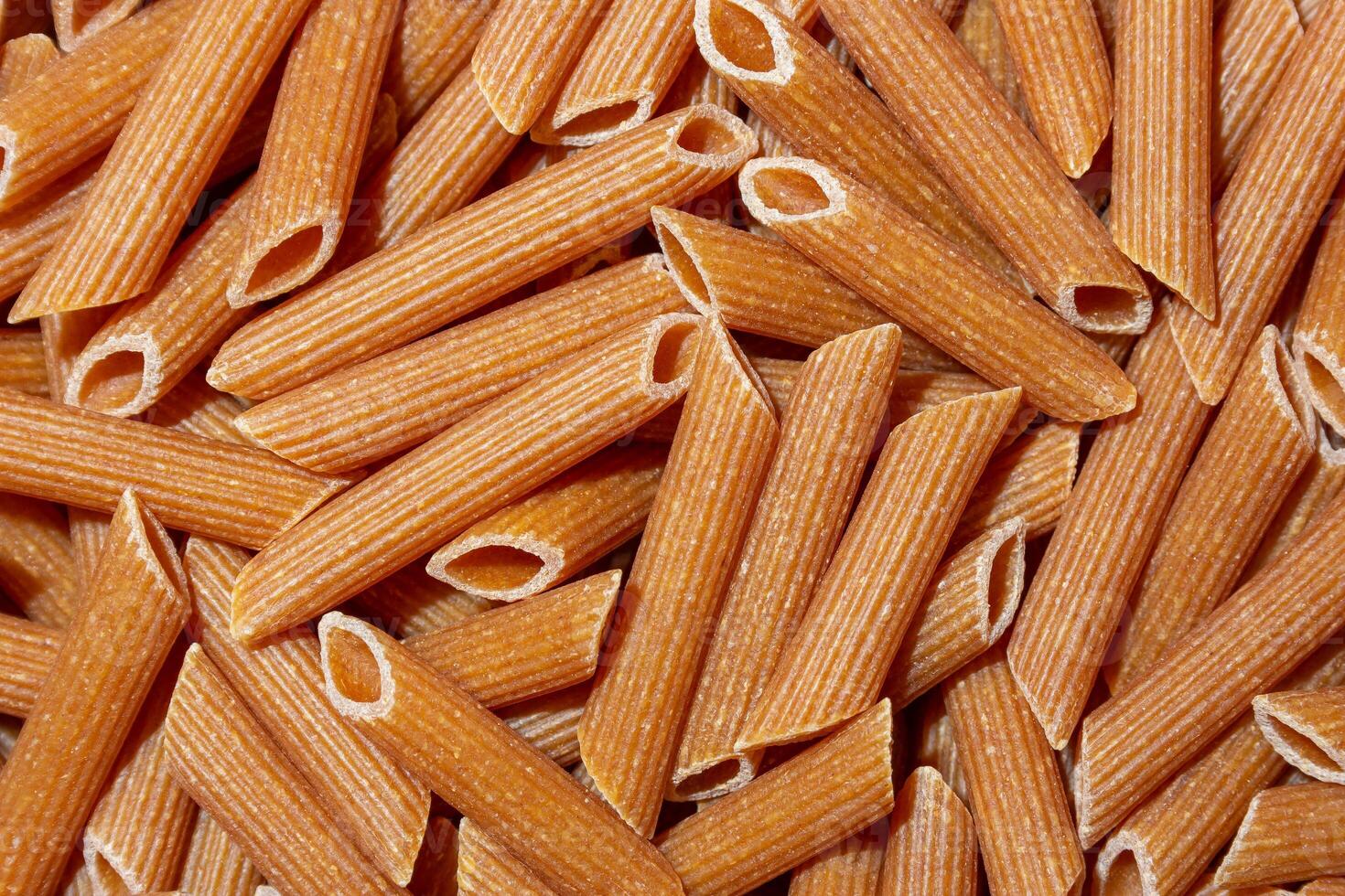 Uncooked Whole Grain Penne Rigate Pasta. A Culinary Canvas of Whole Wheat Macaroni, Creating a Lively and Textured Background for Gourmet Cooking. Whole Grain Dry Pasta. Whole Wheat Raw Macaroni photo