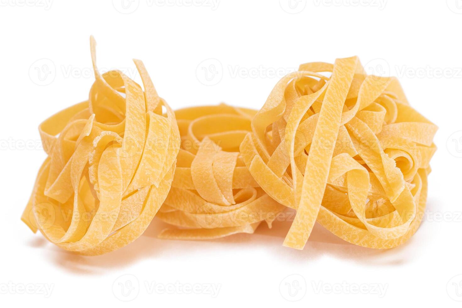 Three Classic Italian Raw Egg Fettuccine - Isolated on White Background. Dry Twisted Uncooked Pasta. Italian Culture and Cuisine. Raw Golden Macaroni Pattern - Isolation photo