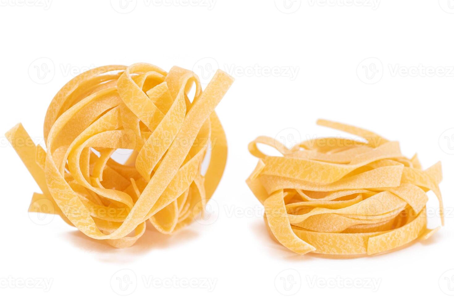 Two Classic Italian Raw Egg Fettuccine - Isolated on White Background. Dry Twisted Uncooked Pasta. Italian Culture and Cuisine. Raw Golden Macaroni Pattern - Isolation photo