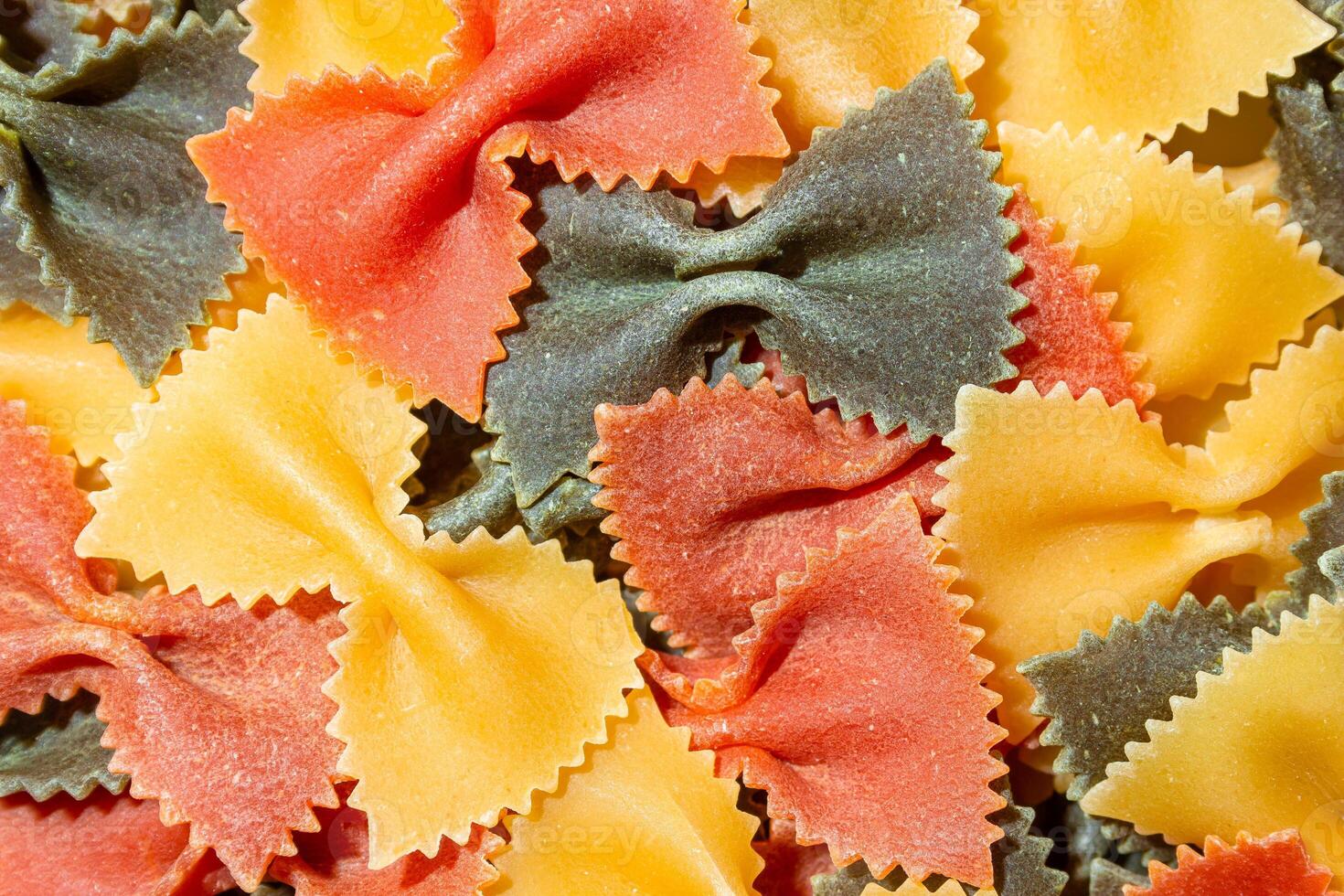 Uncooked Vibrant Colored Farfalle Pasta. A Culinary Canvas of Multicolored Bow-Tie Macaroni, Creating a Lively and Textured Background for Gourmet Cooking Enthusiasts. Colored Dry Pasta. Raw Macaroni photo