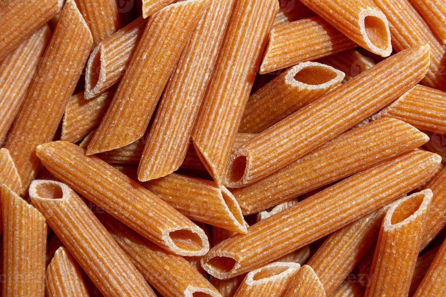 Uncooked Whole Grain Penne Rigate Pasta. A Culinary Canvas of Whole Wheat Macaroni, Creating a Lively and Textured Background for Gourmet Cooking. Whole Grain Dry Pasta. Whole Wheat Raw Macaroni photo