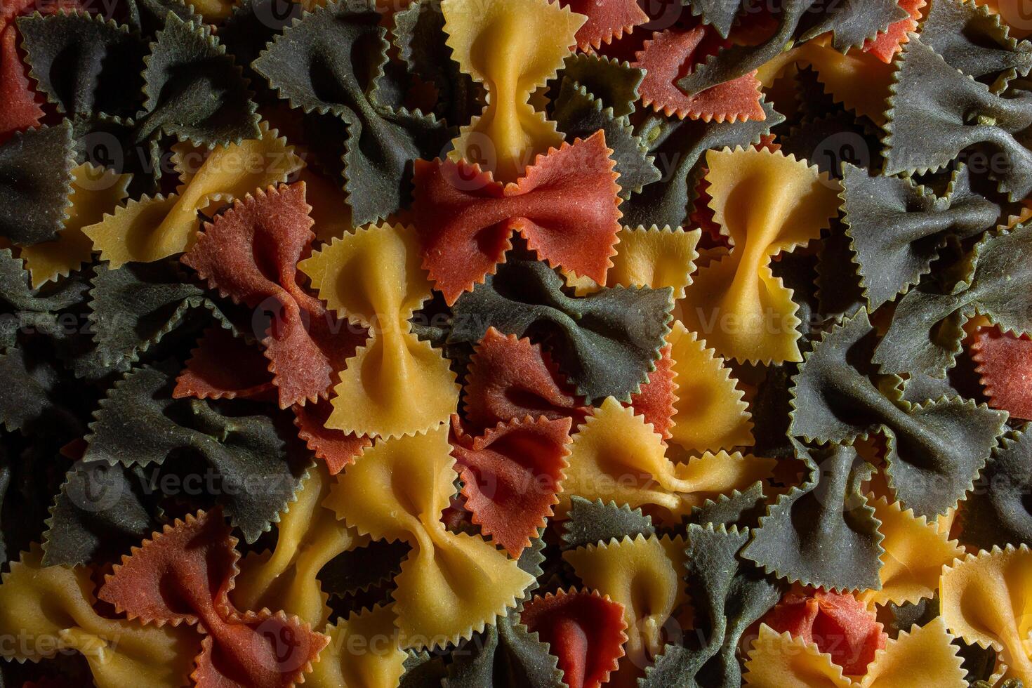Uncooked Vibrant Colored Farfalle Pasta. A Culinary Canvas of Multicolored Bow-Tie Macaroni, Creating a Lively and Textured Background for Gourmet Cooking Enthusiasts. Colored Dry Pasta. Raw Macaroni photo