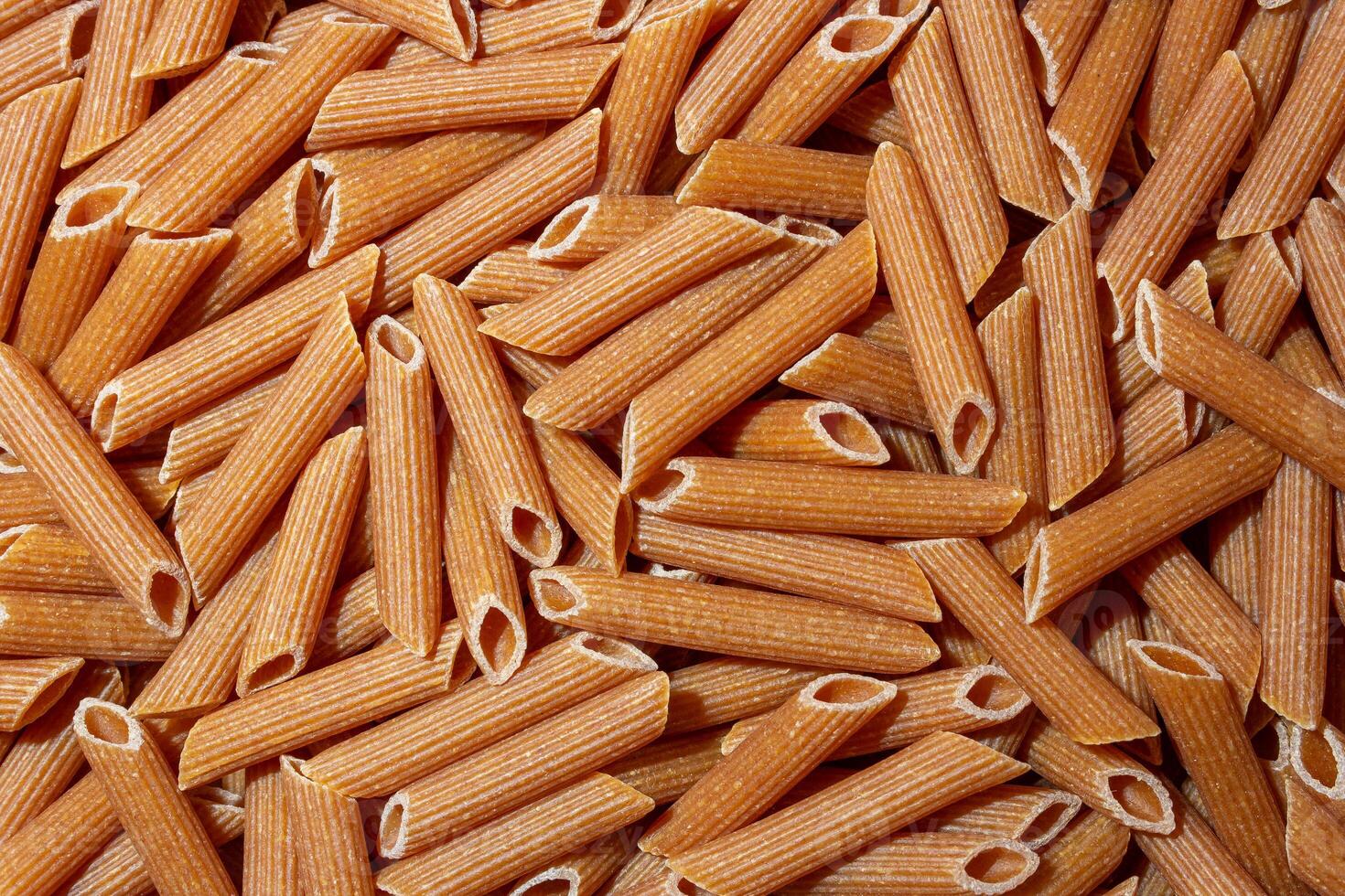 Uncooked Whole Grain Penne Rigate Pasta. A Culinary Canvas of Whole Wheat Macaroni, Creating a Lively and Textured Background for Gourmet Cooking. Whole Grain Dry Pasta. Whole Wheat Raw Macaroni photo