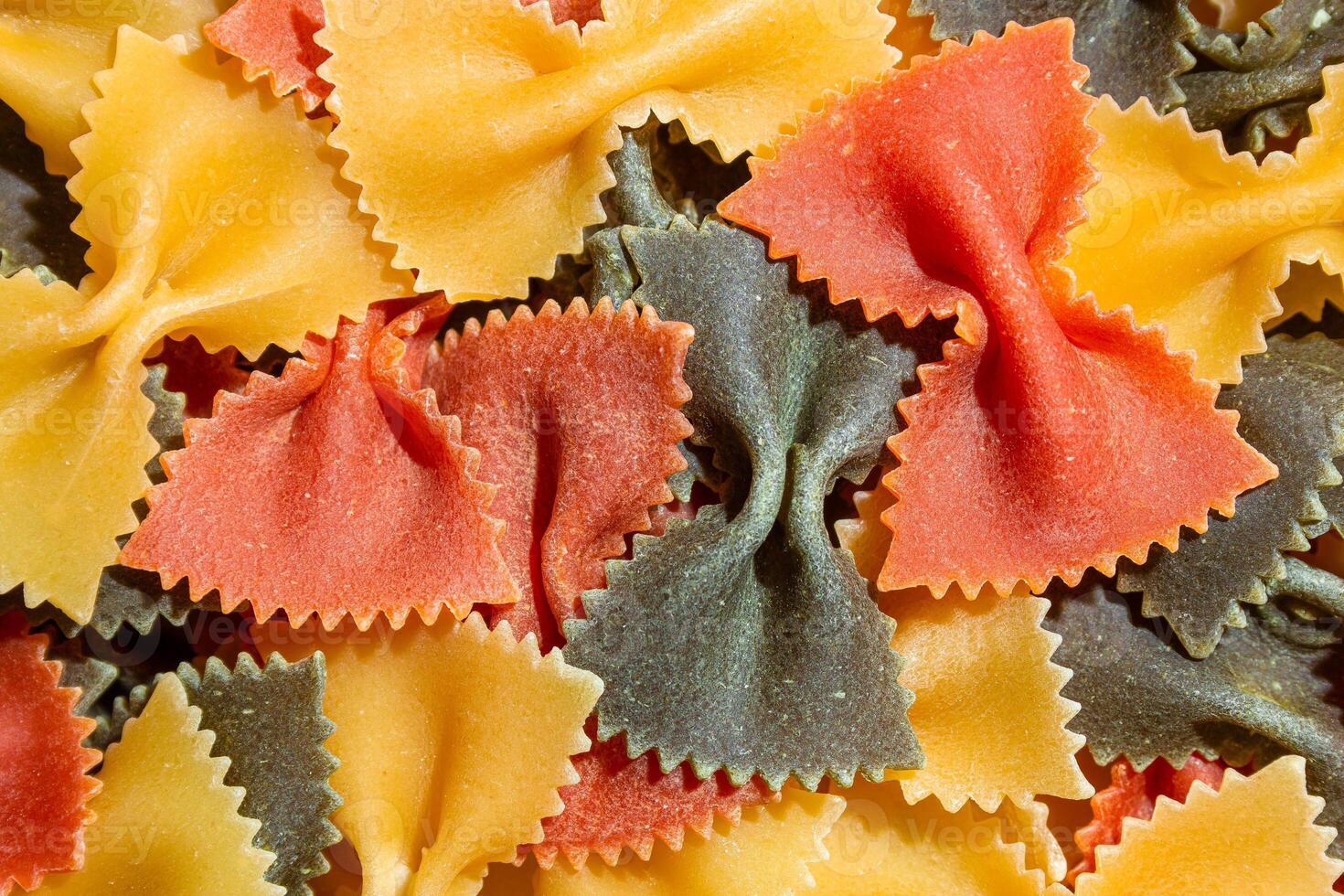 Uncooked Vibrant Colored Farfalle Pasta. A Culinary Canvas of Multicolored Bow-Tie Macaroni, Creating a Lively and Textured Background for Gourmet Cooking Enthusiasts. Colored Dry Pasta. Raw Macaroni photo