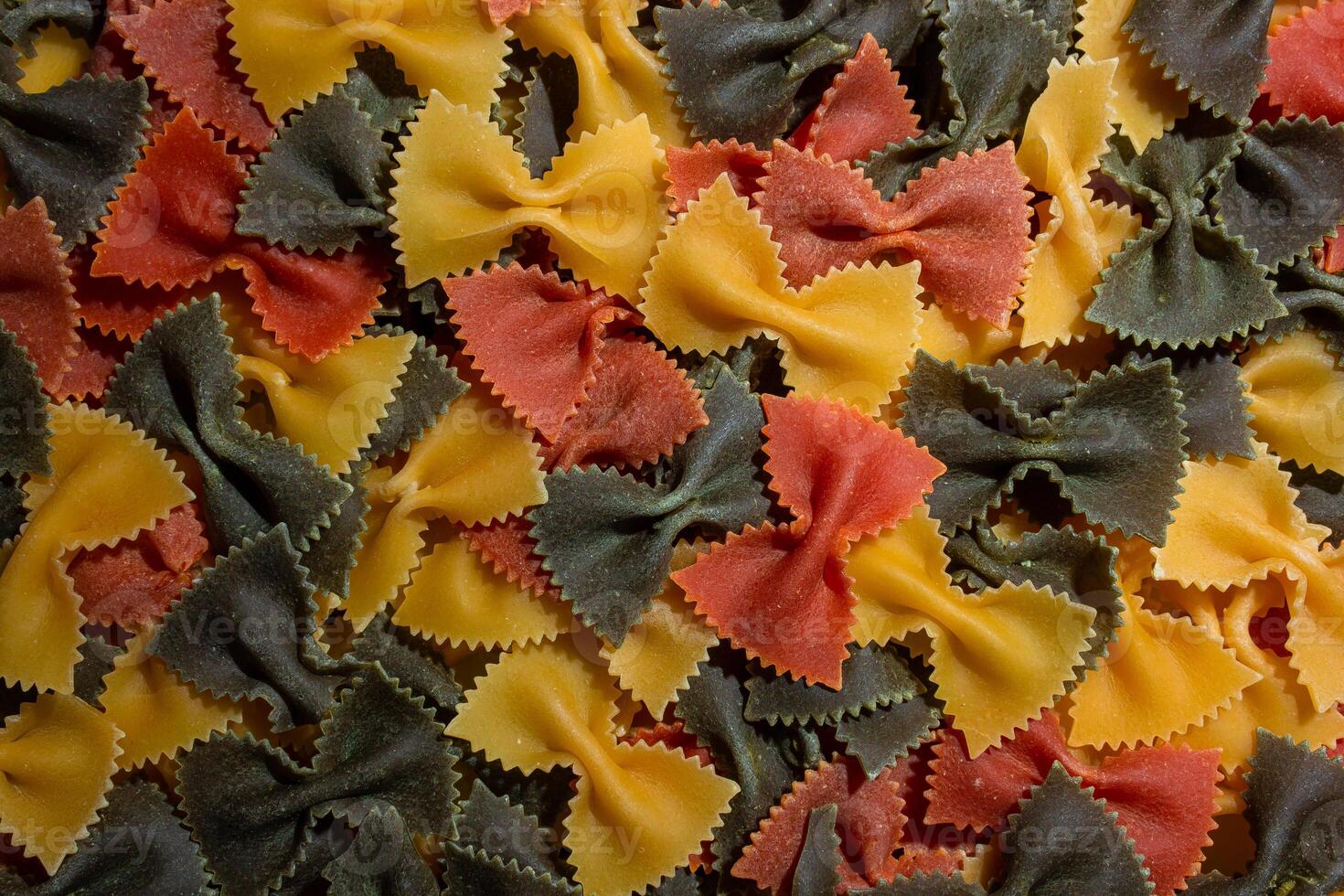 Uncooked Vibrant Colored Farfalle Pasta. A Culinary Canvas of Multicolored Bow-Tie Macaroni, Creating a Lively and Textured Background for Gourmet Cooking Enthusiasts. Colored Dry Pasta. Raw Macaroni photo