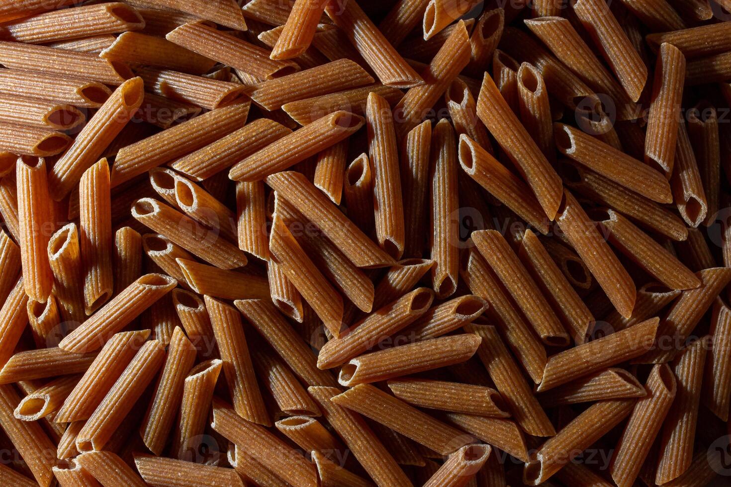 Uncooked Whole Grain Penne Rigate Pasta. A Culinary Canvas of Whole Wheat Macaroni, Creating a Lively and Textured Background for Gourmet Cooking. Whole Grain Dry Pasta. Whole Wheat Raw Macaroni photo