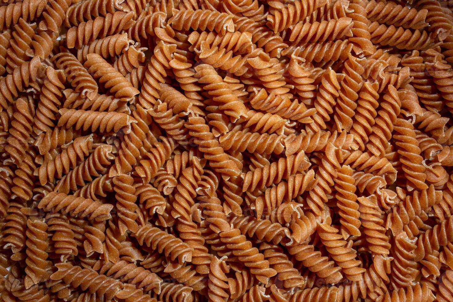 Uncooked Whole Grain Fusilli Pasta. A Culinary Canvas of Whole Wheat Spirals, Creating a Lively and Textured Background for Gourmet Cooking. Whole Grain Twisted Dry Pasta. Whole Wheat Raw Macaroni photo
