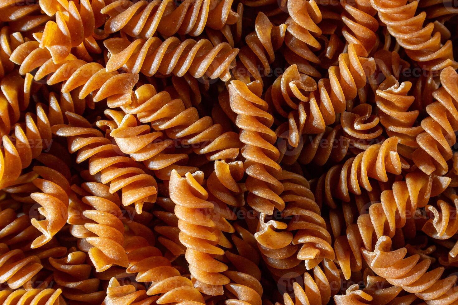 Uncooked Whole Grain Fusilli Pasta. A Culinary Canvas of Whole Wheat Spirals, Creating a Lively and Textured Background for Gourmet Cooking. Whole Grain Twisted Dry Pasta. Whole Wheat Raw Macaroni photo