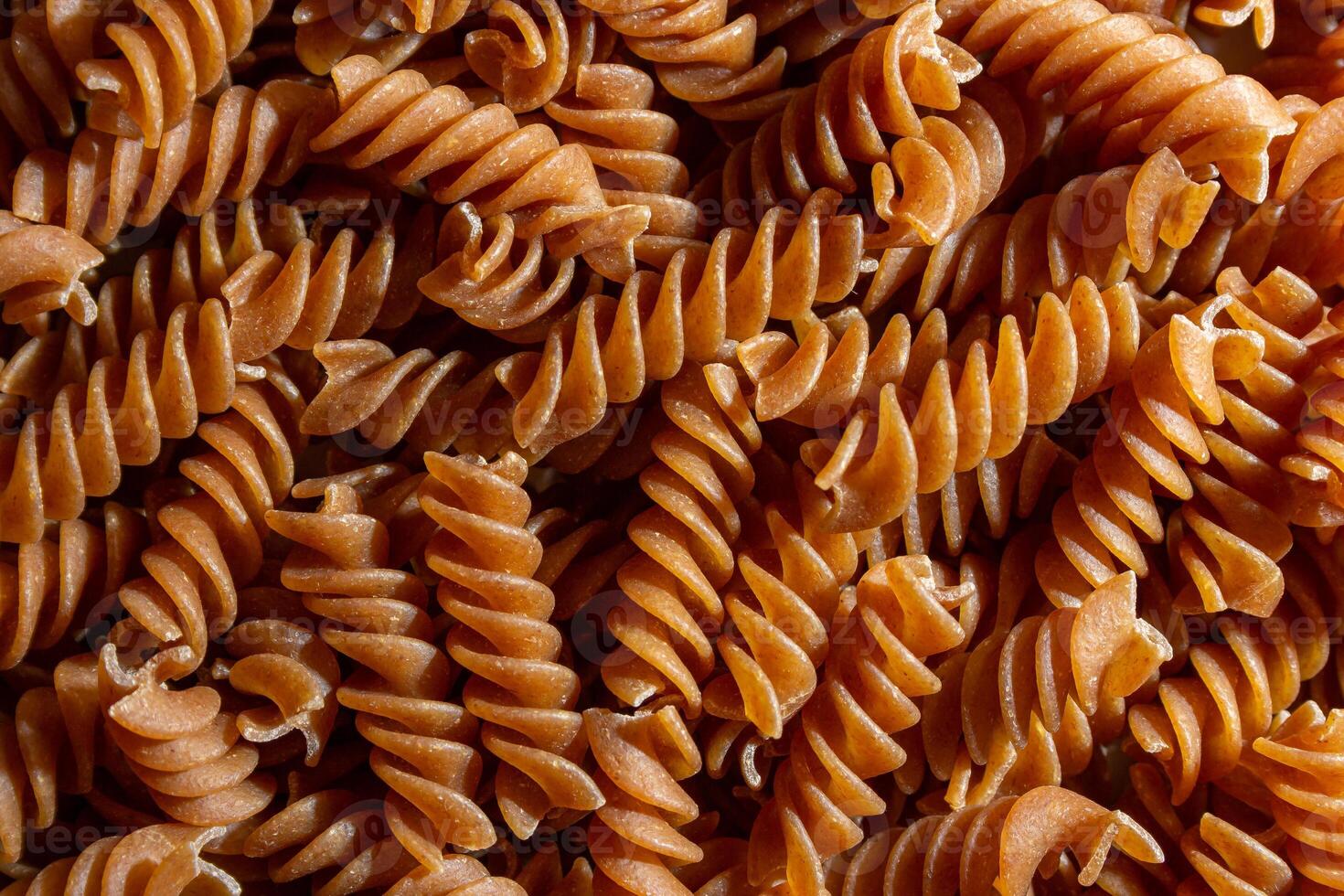 Uncooked Whole Grain Fusilli Pasta. A Culinary Canvas of Whole Wheat Spirals, Creating a Lively and Textured Background for Gourmet Cooking. Whole Grain Twisted Dry Pasta. Whole Wheat Raw Macaroni photo