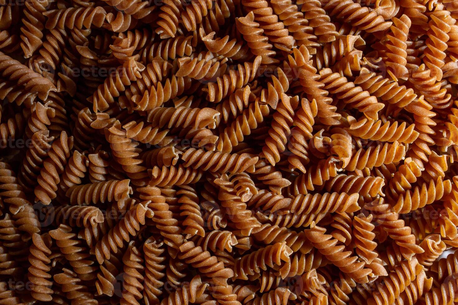 Uncooked Whole Grain Fusilli Pasta. A Culinary Canvas of Whole Wheat Spirals, Creating a Lively and Textured Background for Gourmet Cooking. Whole Grain Twisted Dry Pasta. Whole Wheat Raw Macaroni photo
