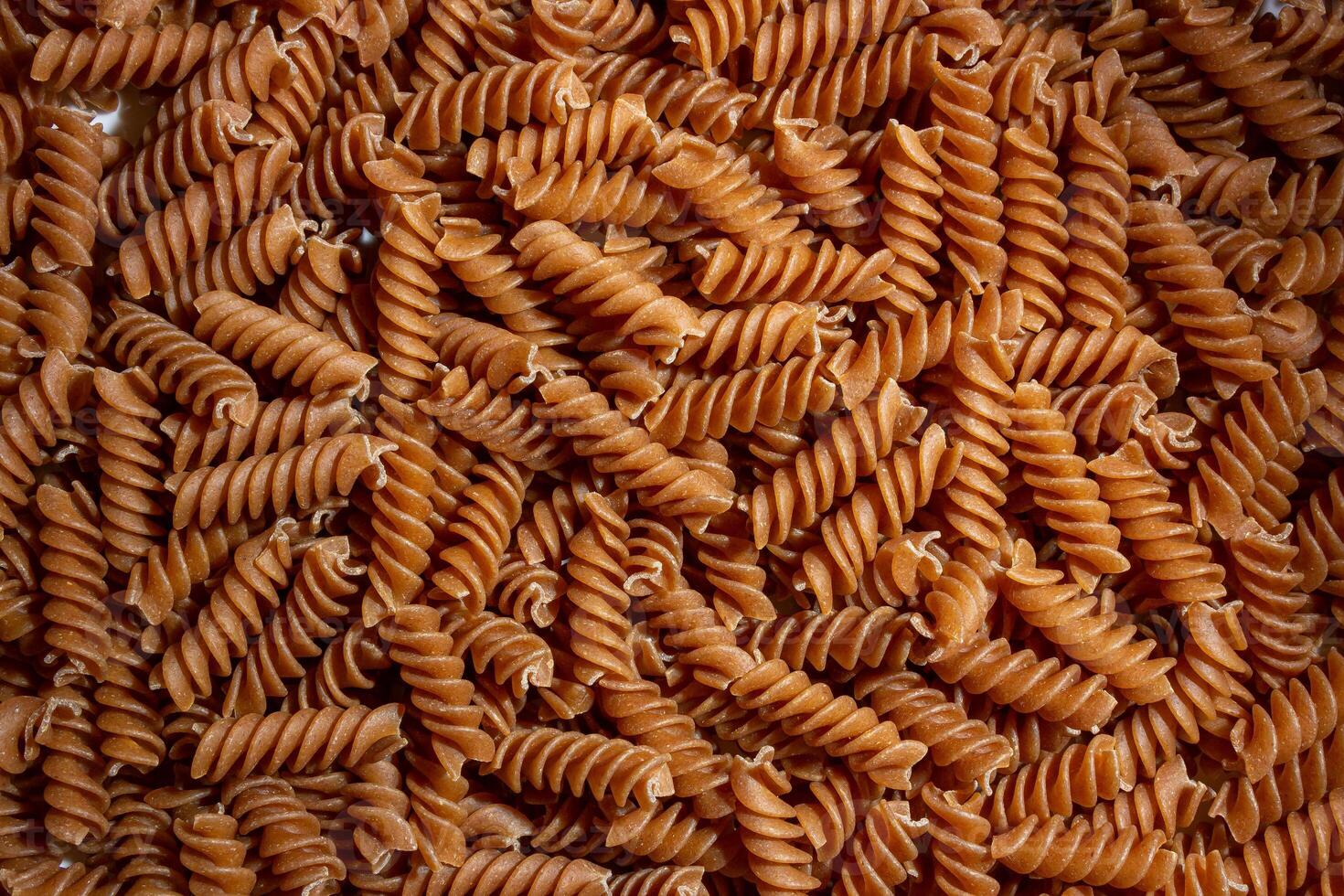 Uncooked Whole Grain Fusilli Pasta. A Culinary Canvas of Whole Wheat Spirals, Creating a Lively and Textured Background for Gourmet Cooking. Whole Grain Twisted Dry Pasta. Whole Wheat Raw Macaroni photo