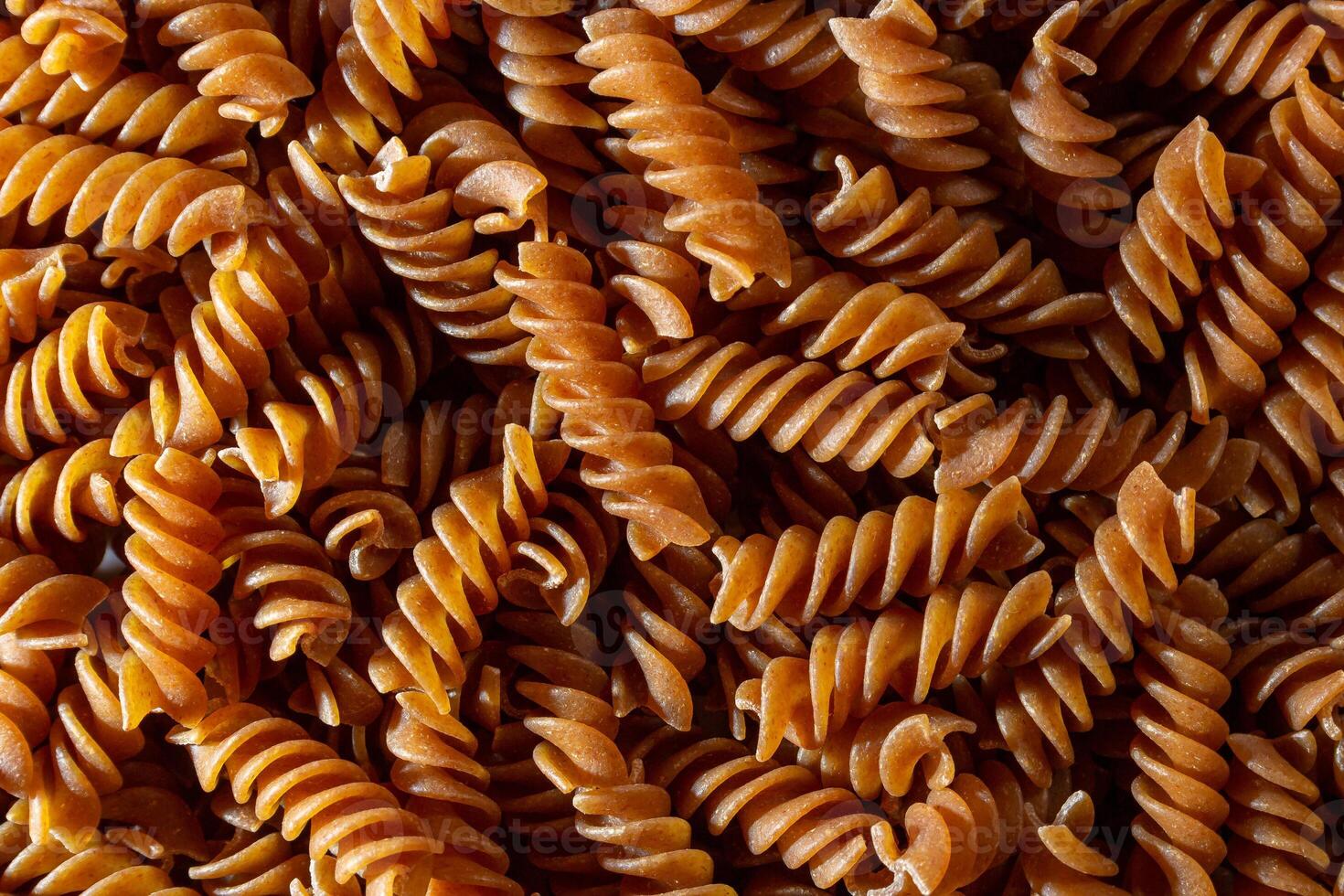 Uncooked Whole Grain Fusilli Pasta. A Culinary Canvas of Whole Wheat Spirals, Creating a Lively and Textured Background for Gourmet Cooking. Whole Grain Twisted Dry Pasta. Whole Wheat Raw Macaroni photo