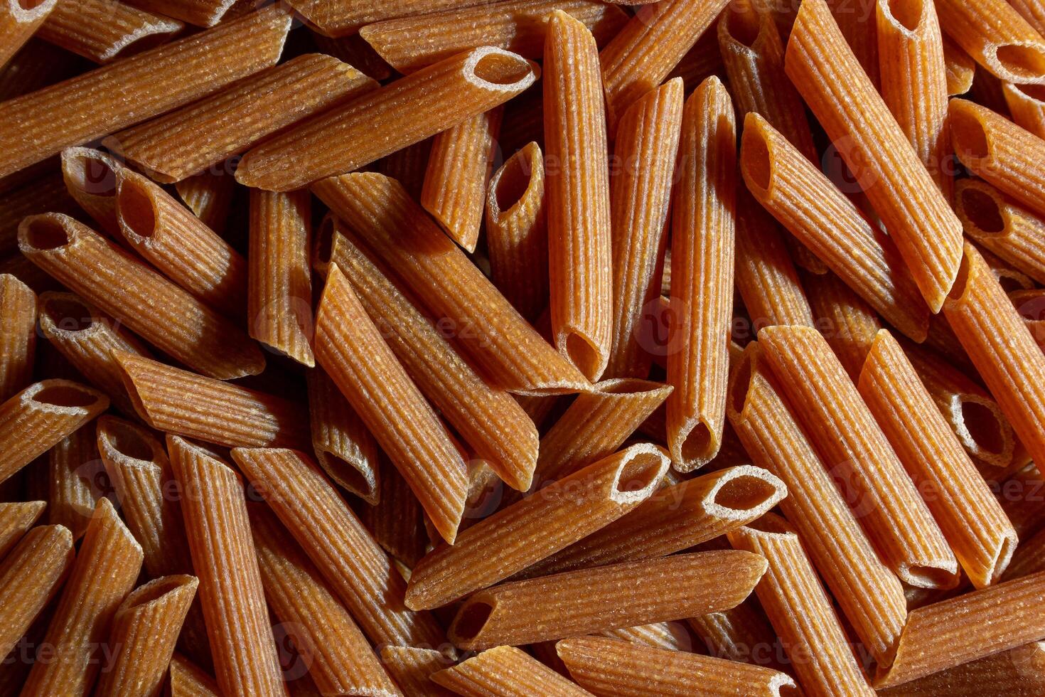 Uncooked Whole Grain Penne Rigate Pasta. A Culinary Canvas of Whole Wheat Macaroni, Creating a Lively and Textured Background for Gourmet Cooking. Whole Grain Dry Pasta. Whole Wheat Raw Macaroni photo