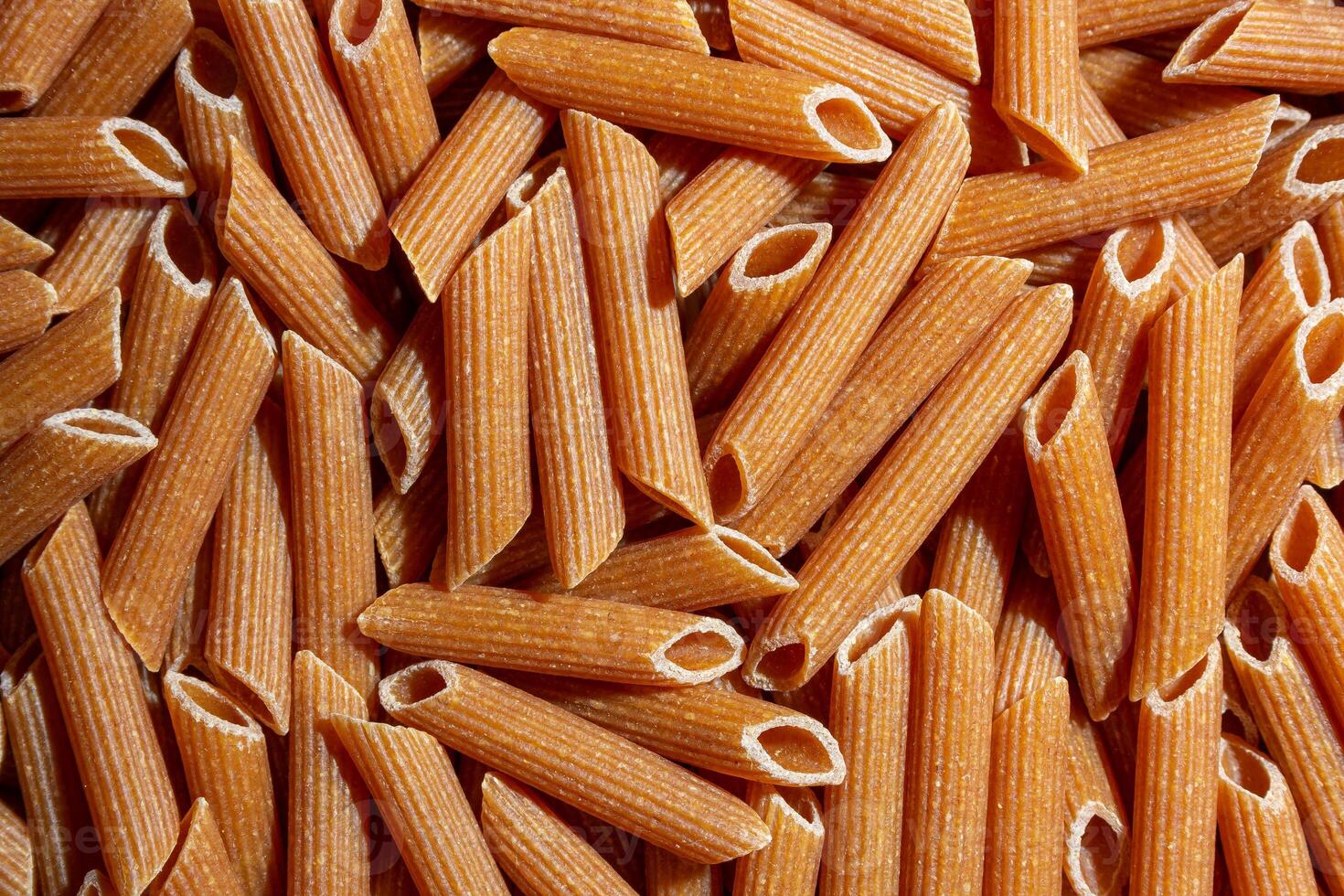 Uncooked Whole Grain Penne Rigate Pasta. A Culinary Canvas of Whole Wheat Macaroni, Creating a Lively and Textured Background for Gourmet Cooking. Whole Grain Dry Pasta. Whole Wheat Raw Macaroni photo