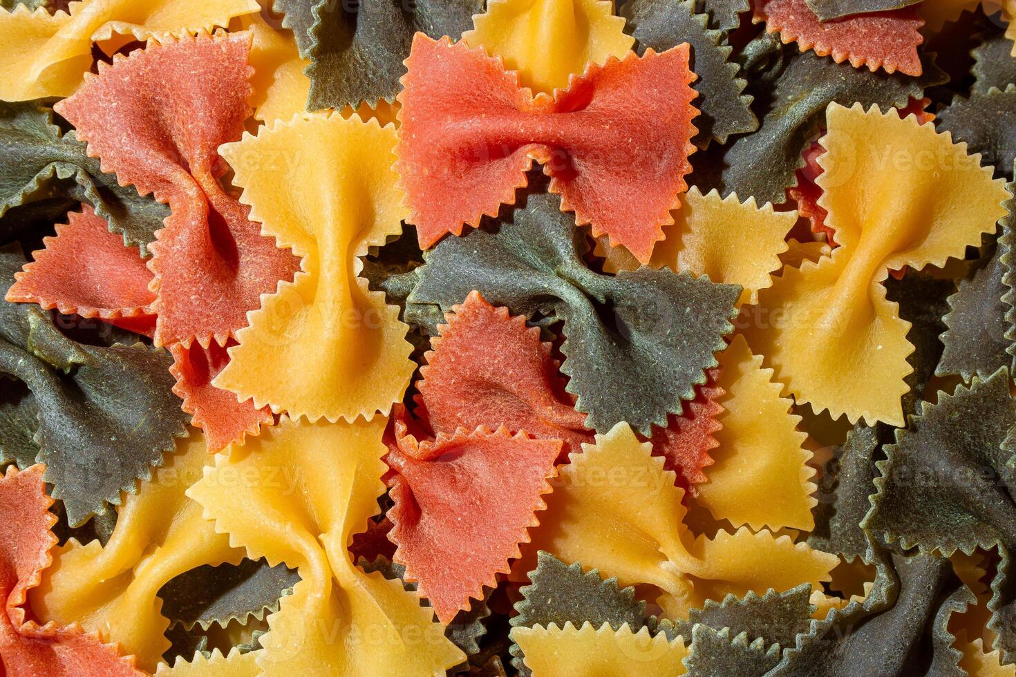 Uncooked Vibrant Colored Farfalle Pasta. A Culinary Canvas of Multicolored Bow-Tie Macaroni, Creating a Lively and Textured Background for Gourmet Cooking Enthusiasts. Colored Dry Pasta. Raw Macaroni photo