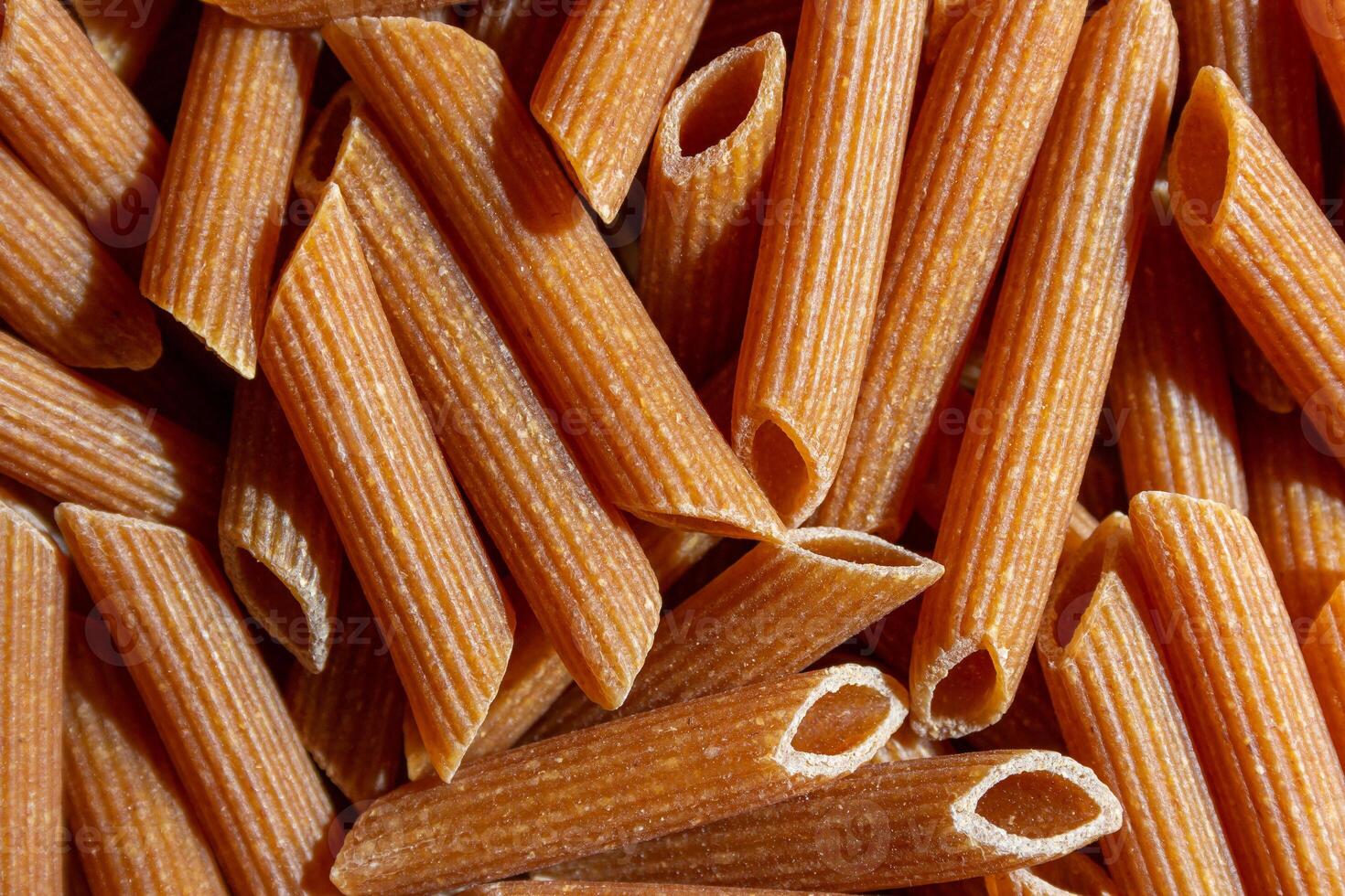 Uncooked Whole Grain Penne Rigate Pasta. A Culinary Canvas of Whole Wheat Macaroni, Creating a Lively and Textured Background for Gourmet Cooking. Whole Grain Dry Pasta. Whole Wheat Raw Macaroni photo