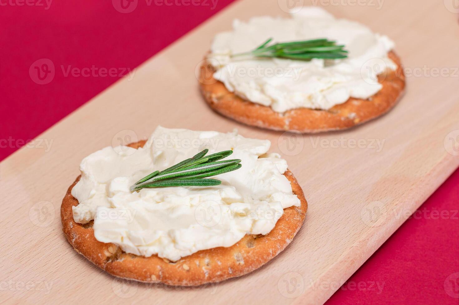 Crispy Cracker Sandwich with Cream Cheese and Rosemary on Wooden Cooking Board on Magenta Background photo