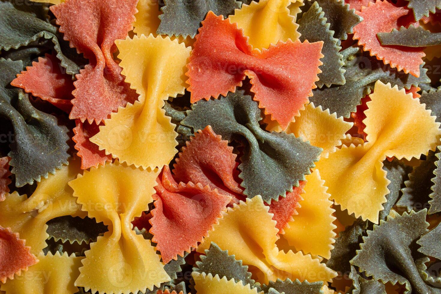 Uncooked Vibrant Colored Farfalle Pasta. A Culinary Canvas of Multicolored Bow-Tie Macaroni, Creating a Lively and Textured Background for Gourmet Cooking Enthusiasts. Colored Dry Pasta. Raw Macaroni photo