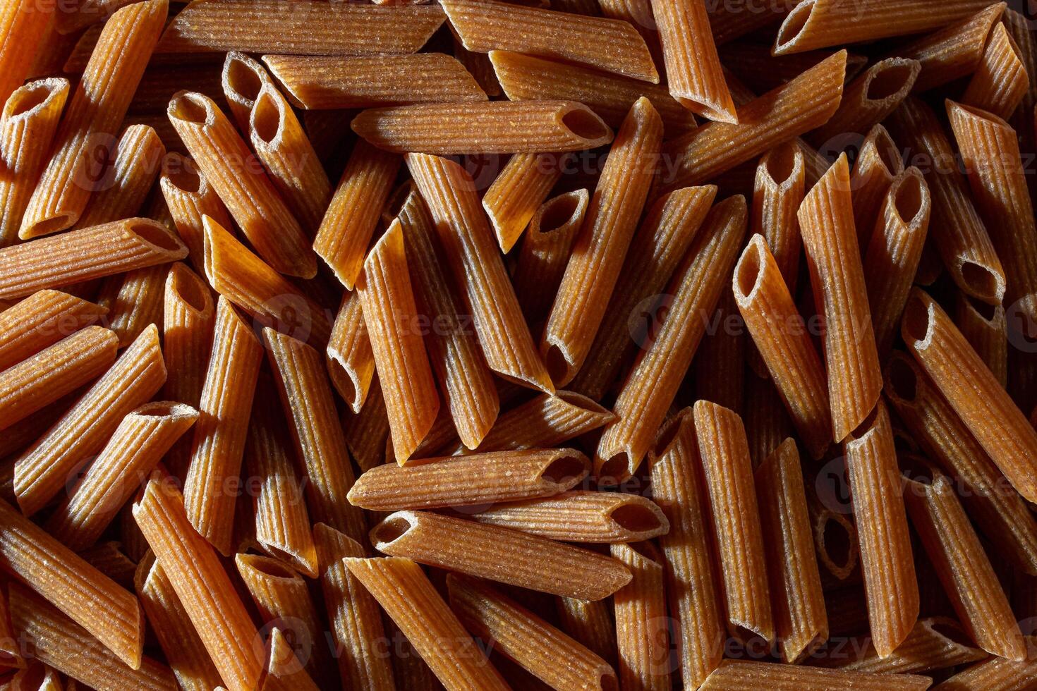 Uncooked Whole Grain Penne Rigate Pasta. A Culinary Canvas of Whole Wheat Macaroni, Creating a Lively and Textured Background for Gourmet Cooking. Whole Grain Dry Pasta. Whole Wheat Raw Macaroni photo