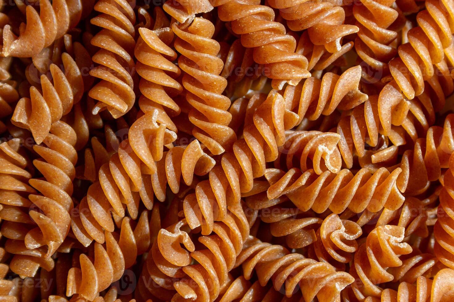 Uncooked Whole Grain Fusilli Pasta. A Culinary Canvas of Whole Wheat Spirals, Creating a Lively and Textured Background for Gourmet Cooking. Whole Grain Twisted Dry Pasta. Whole Wheat Raw Macaroni photo