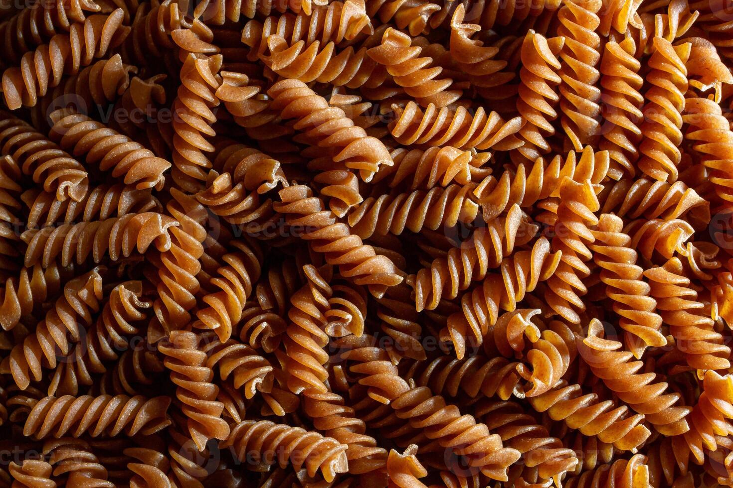 Uncooked Whole Grain Fusilli Pasta. A Culinary Canvas of Whole Wheat Spirals, Creating a Lively and Textured Background for Gourmet Cooking. Whole Grain Twisted Dry Pasta. Whole Wheat Raw Macaroni photo