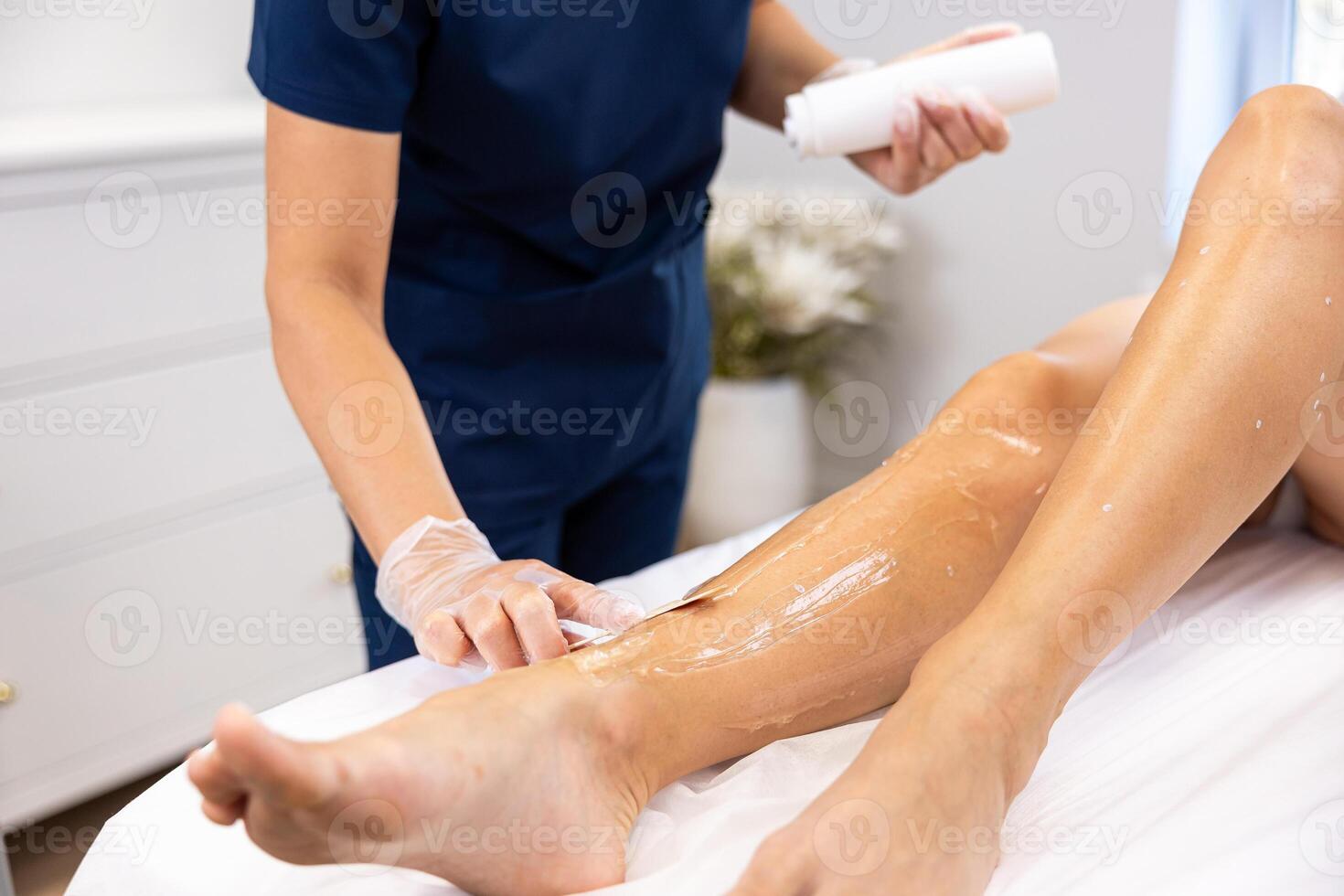 Professional leg waxing treatment at a beauty spa, with a beautician applying wax using a wooden spatula photo
