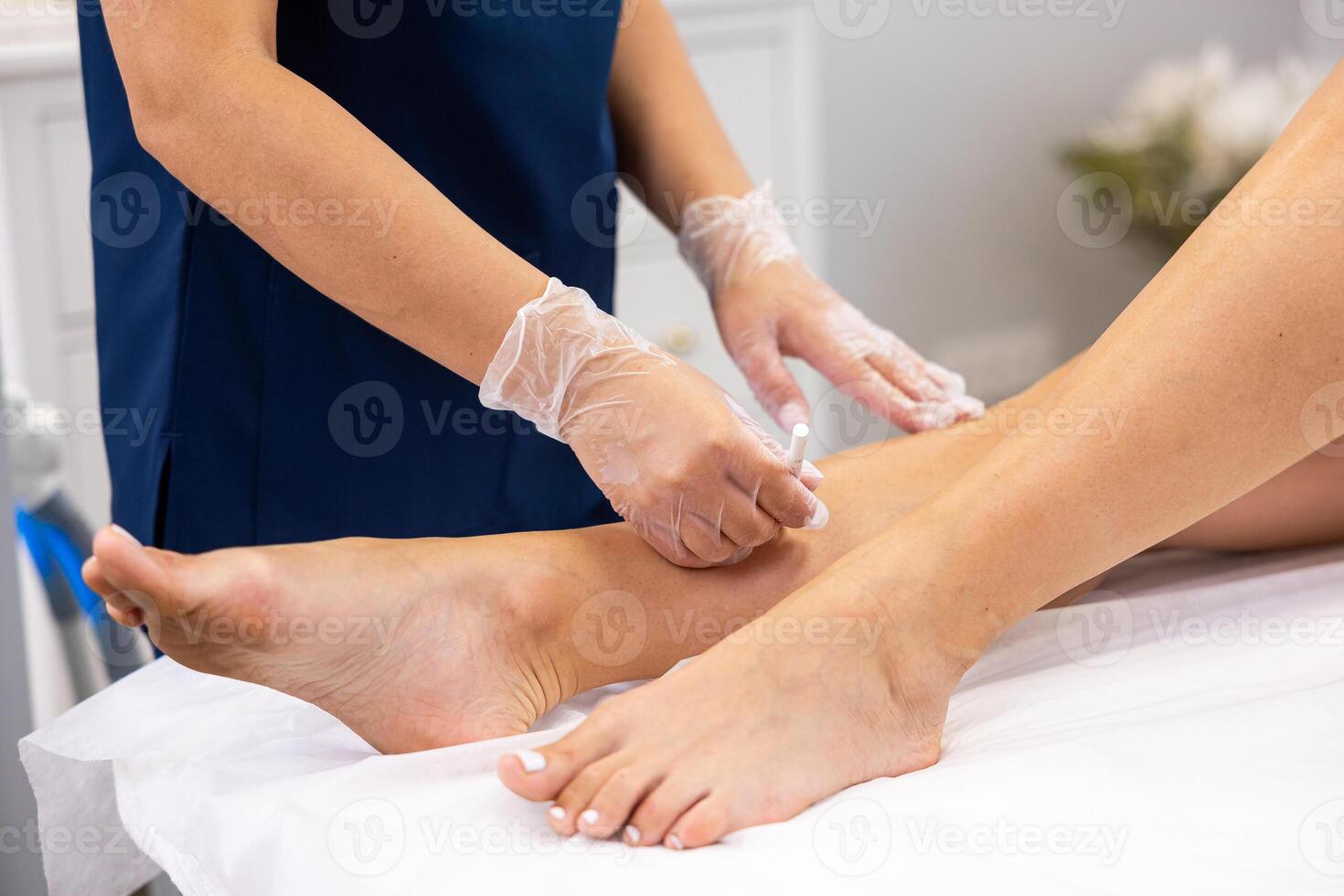 Professional beautician marking birthmarks with a white pencil during a leg waxing procedure in a beauty salon photo