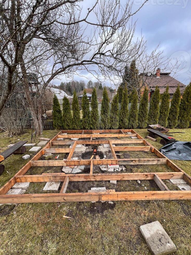 Framework of a wooden deck under construction in a backyard with trees and greenery in the background. photo